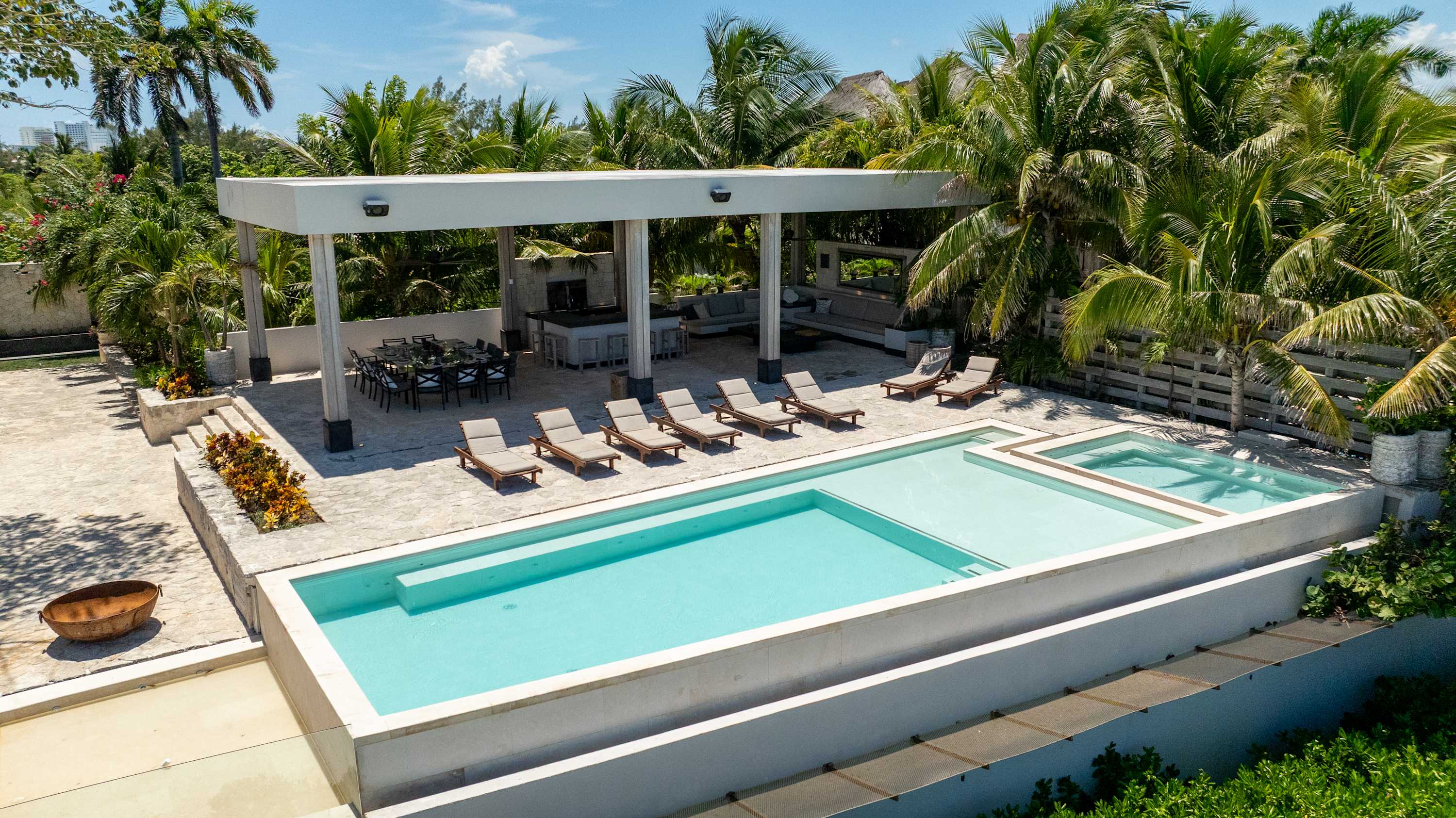Modern villa with infinity pool, outdoor dining, and lounge area amidst palm trees.