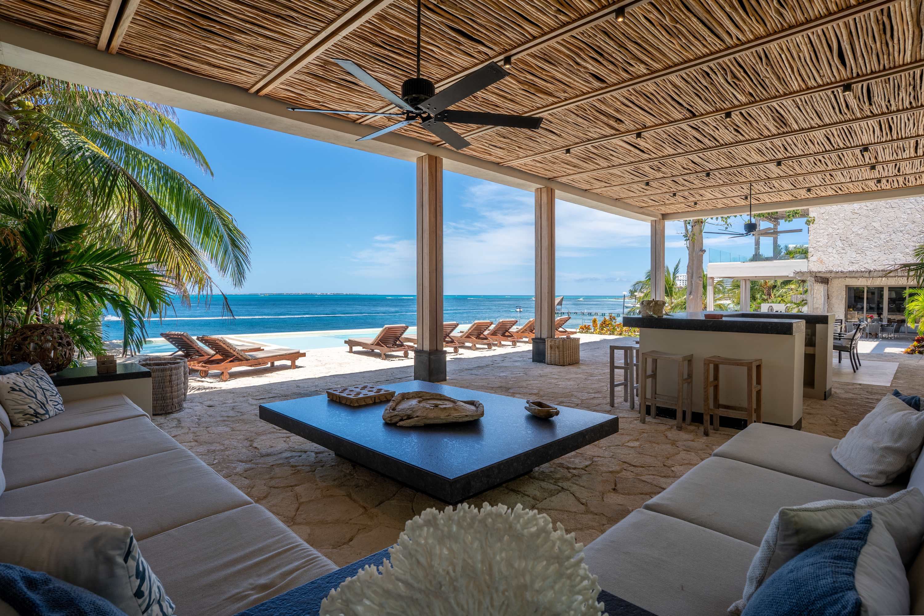 Outdoor living area with sofas, coffee table, bar, and ocean view.