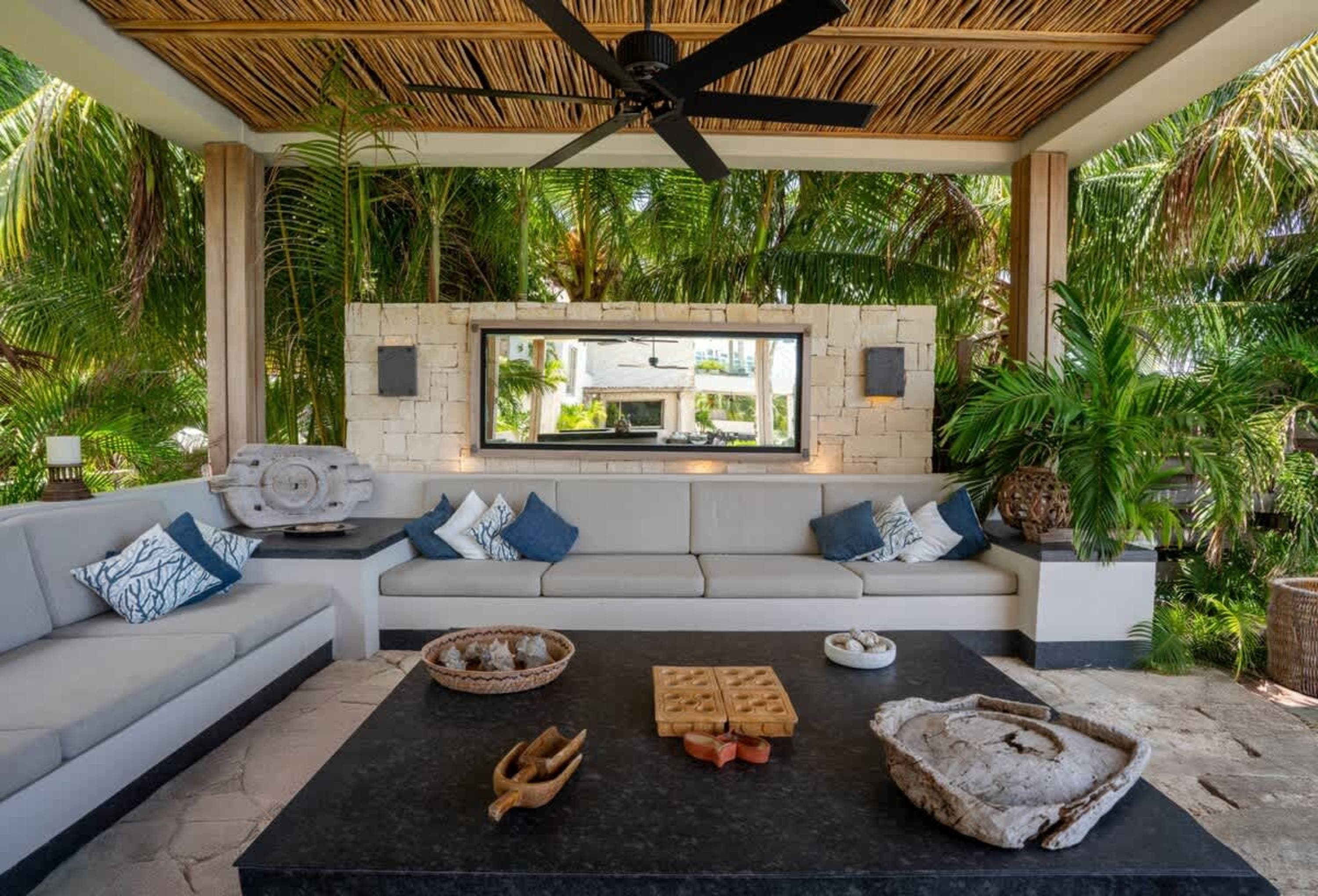 Outdoor living room with a thatched roof, ceiling fan, sectional sofa, and coffee table.