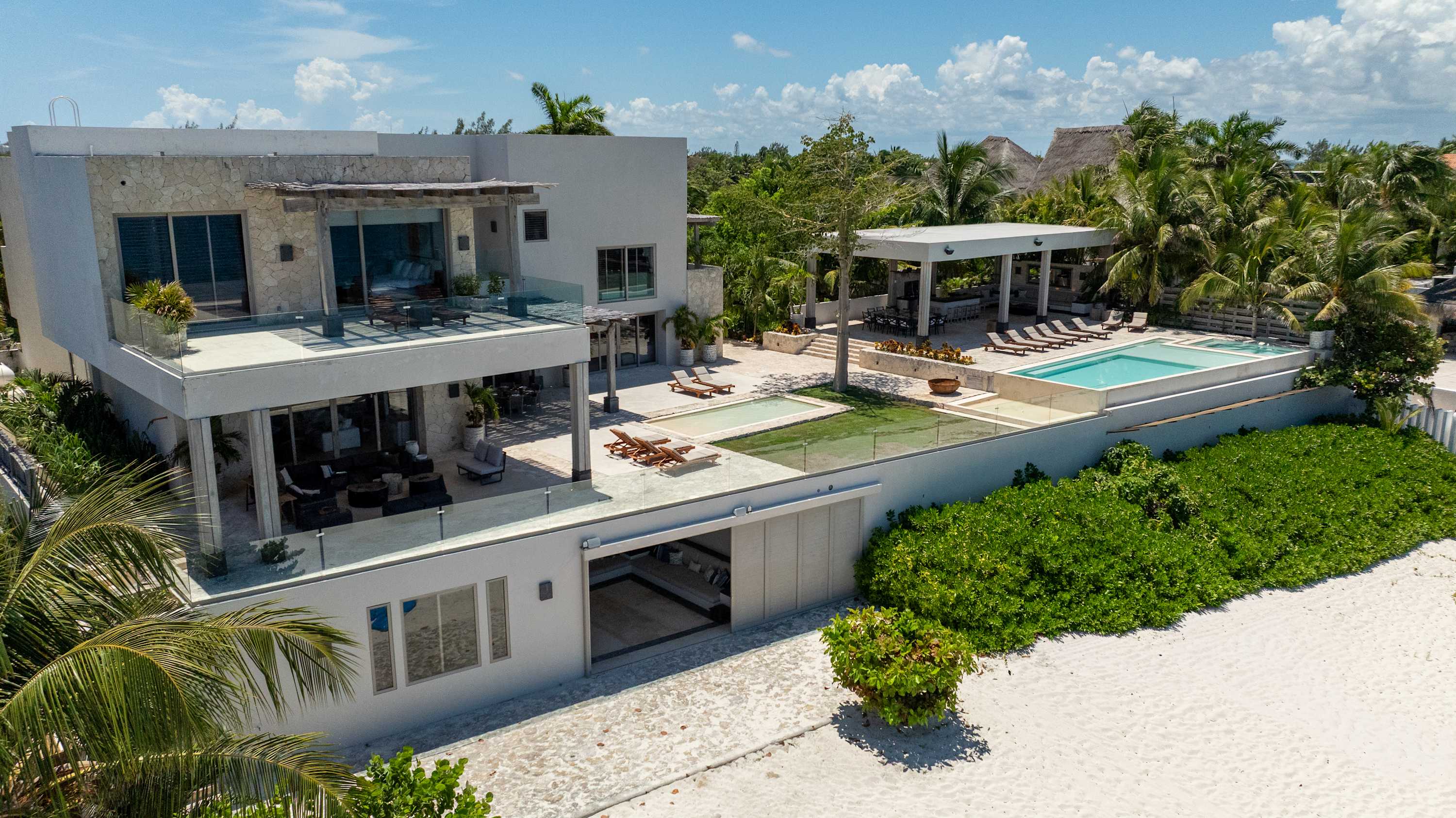 A modern white villa with a pool, outdoor seating, and lush tropical landscaping on a sandy beach.
