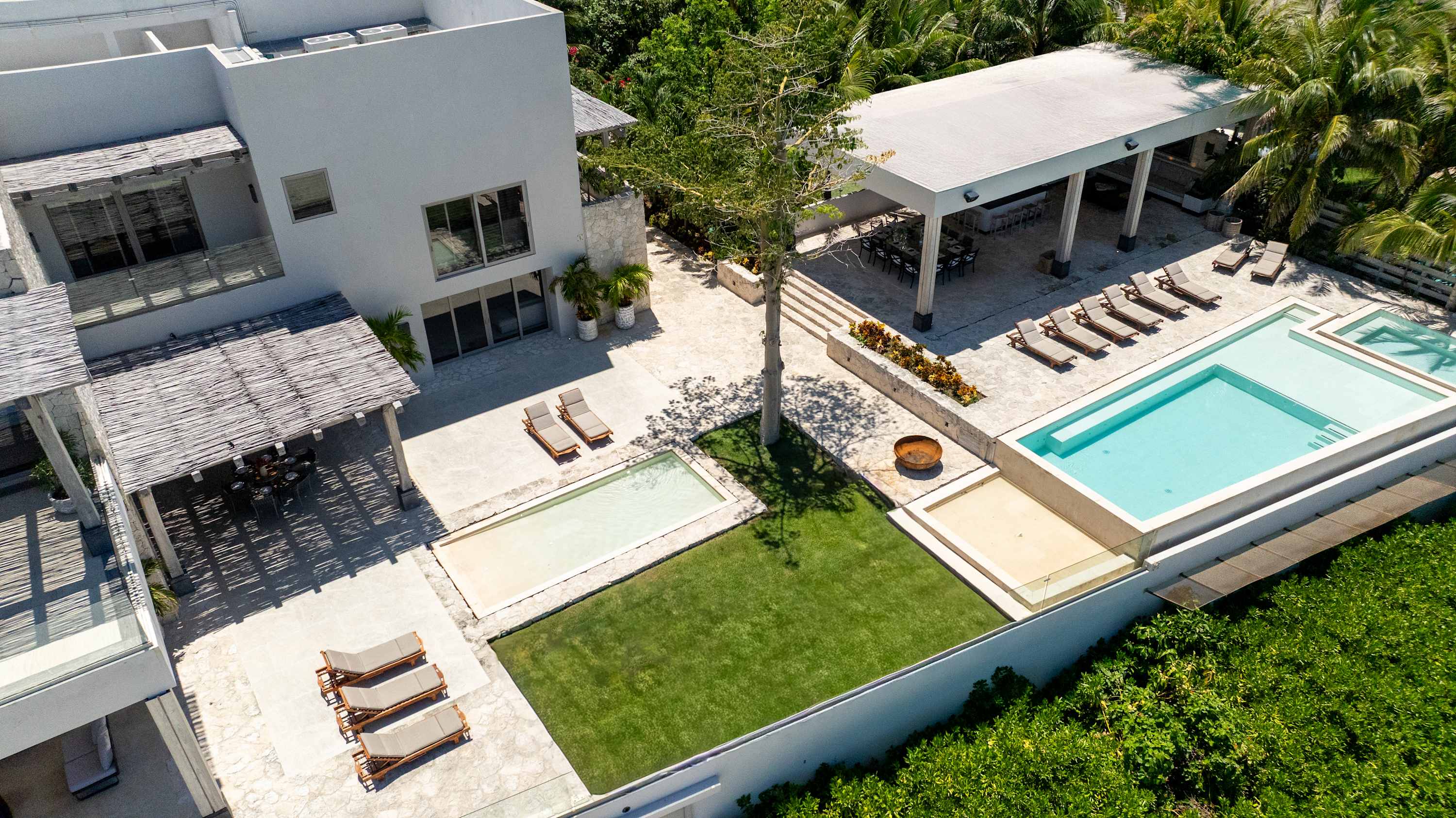 Modern villa with multiple pools, lounge chairs, outdoor dining, and lush greenery.