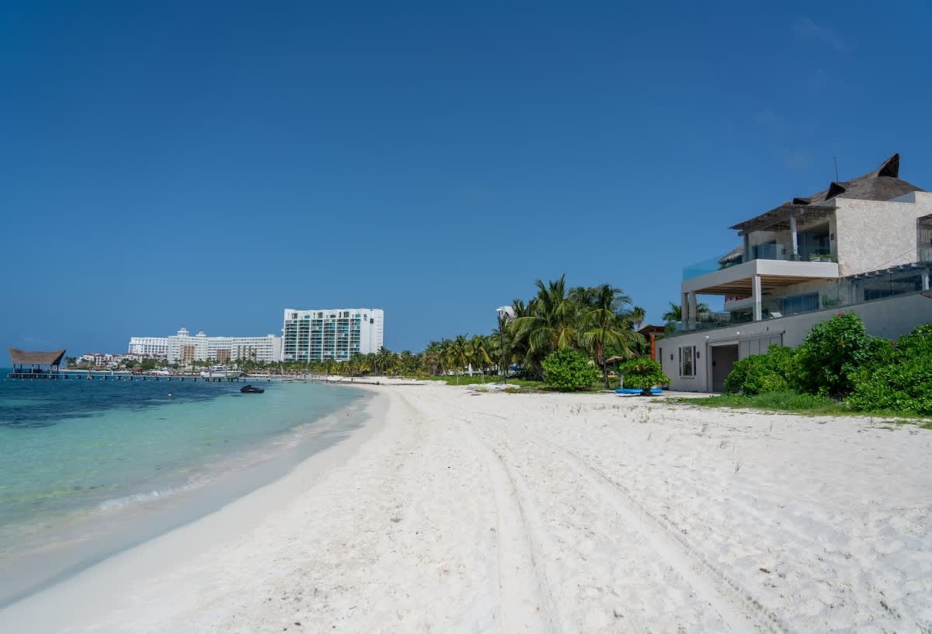 A pristine white sand beach stretches towards a crystal-clear turquoise ocean under a bright blue sk