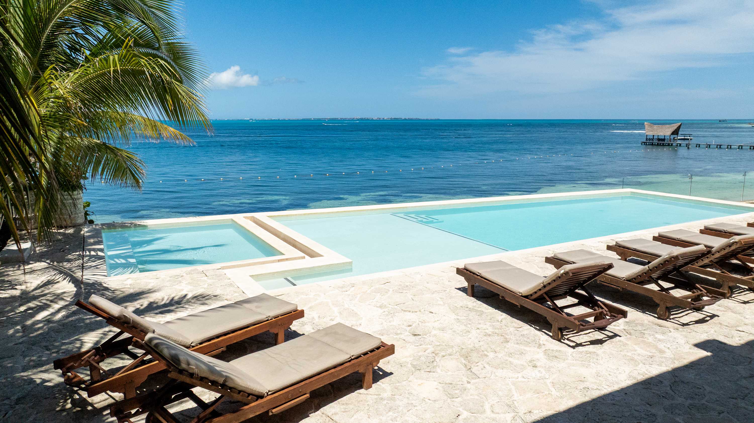 Sun loungers face a beautiful infinity pool overlooking a tropical ocean.