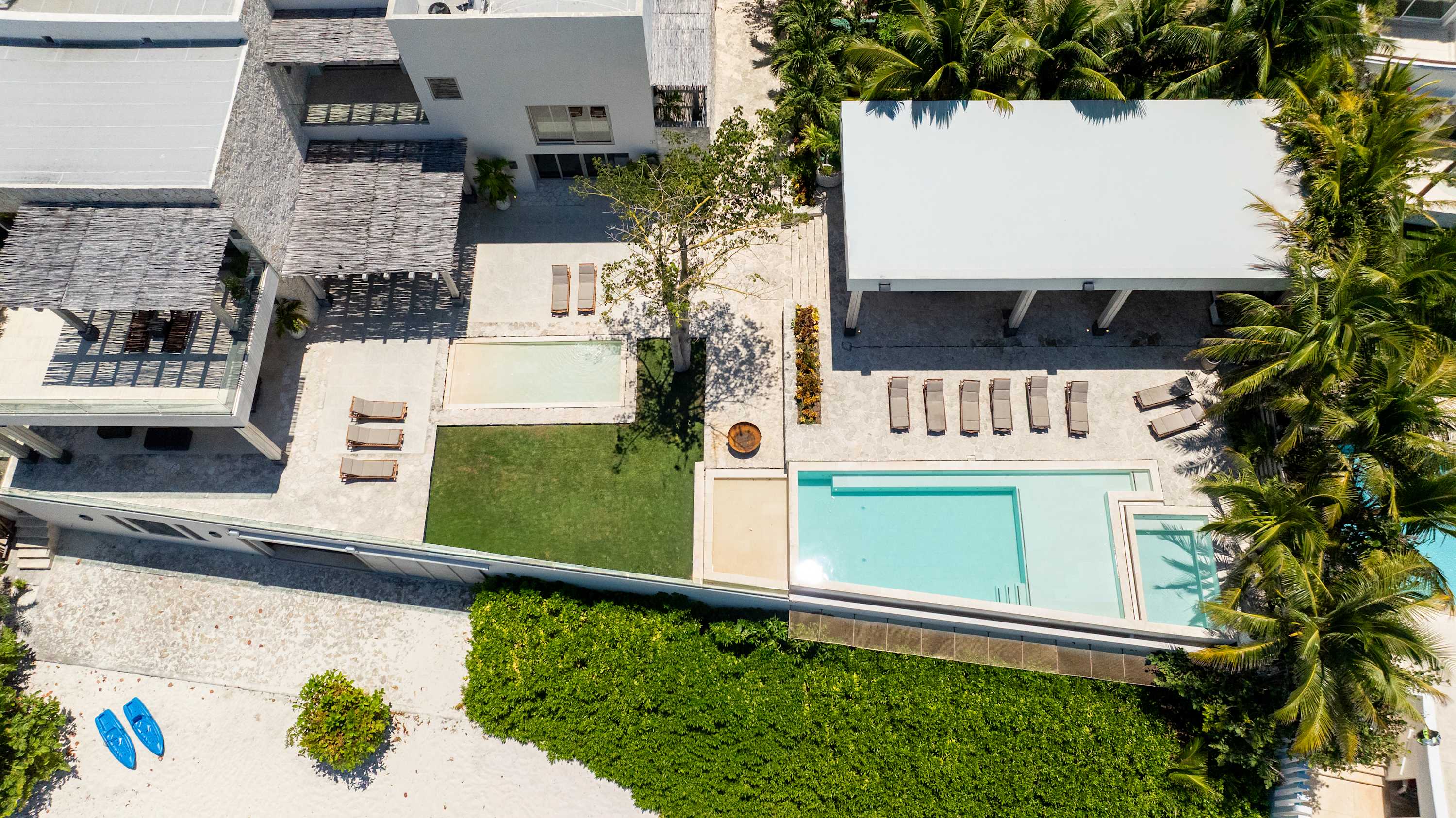 An aerial view of a modern villa with multiple pools, lounge chairs, and palm trees.