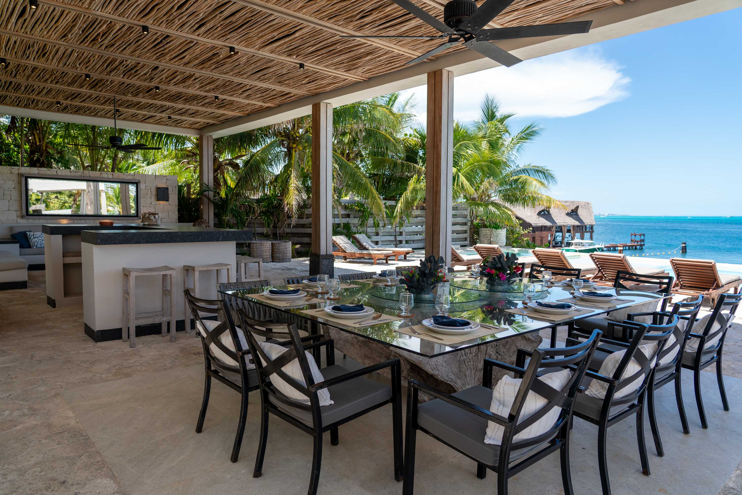 Outdoor dining area with a glass table, chairs, and a view of the ocean.