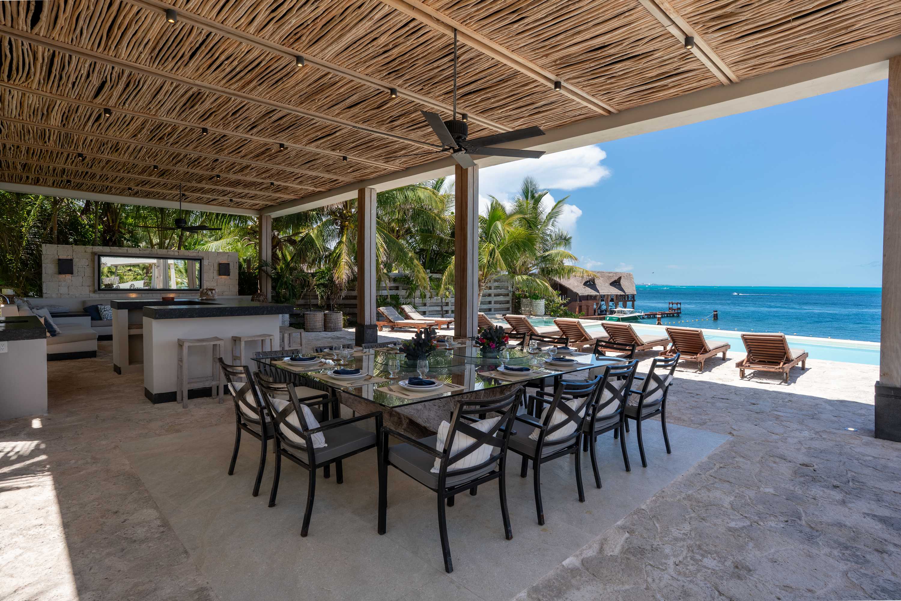 An outdoor dining area with a glass table and chairs, a kitchen, and a view of the ocean.