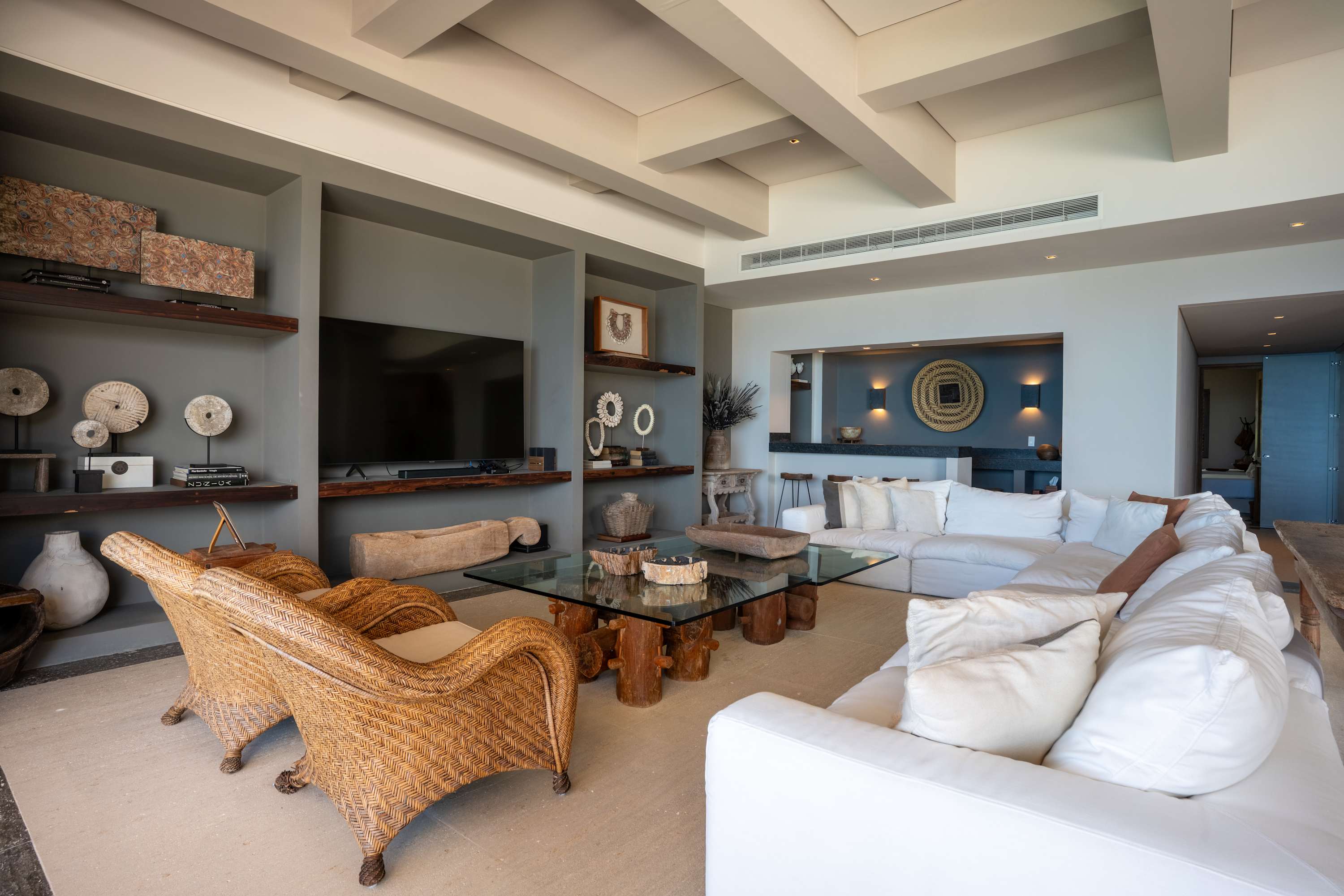 A living room with rattan chairs and white sofas around a glass coffee table.