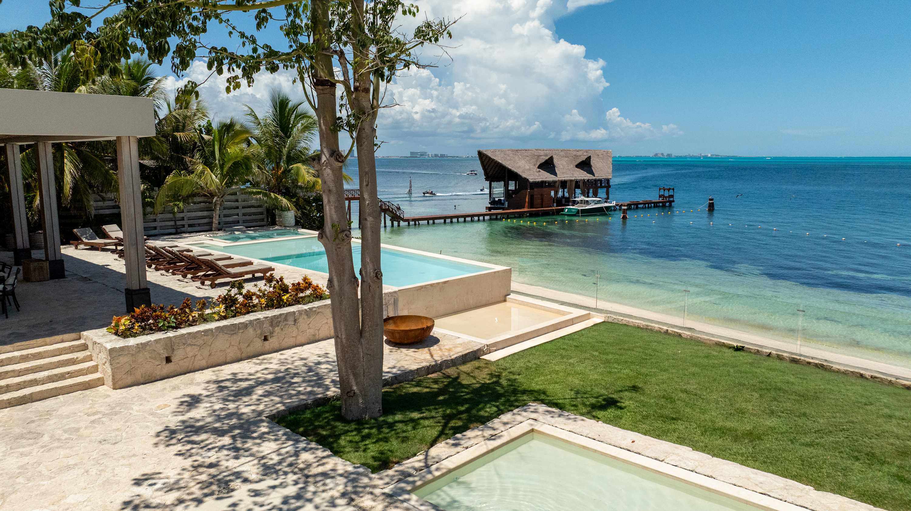 Tropical resort with infinity pools, palm trees, and a thatched-roof overwater bar with a boat.