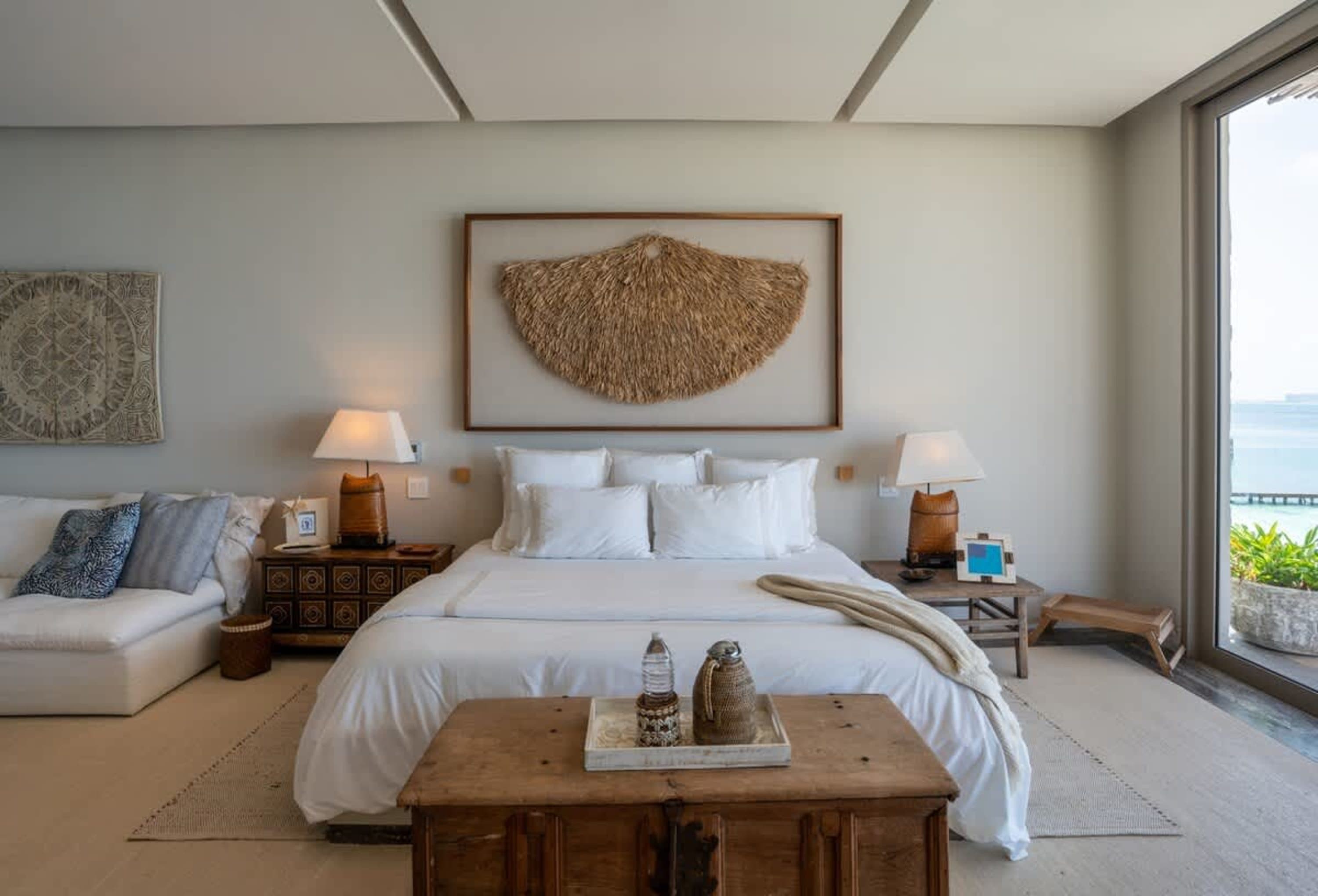 A bedroom with a large bed, white bedding, and a decorative piece of artwork on the wall.