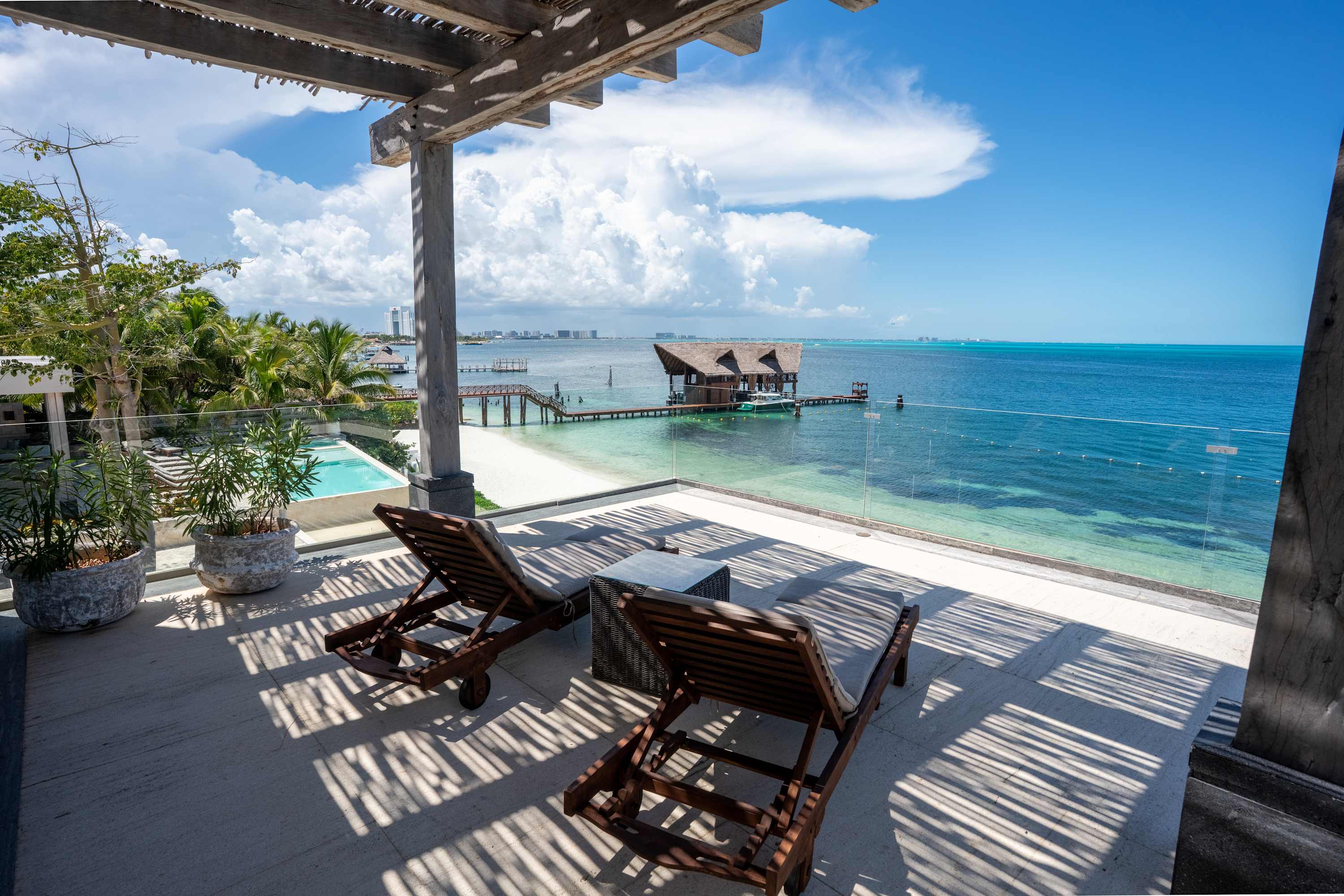 Beachfront patio with lounge chairs overlooking a tropical ocean and a thatched-roof overwater bunga