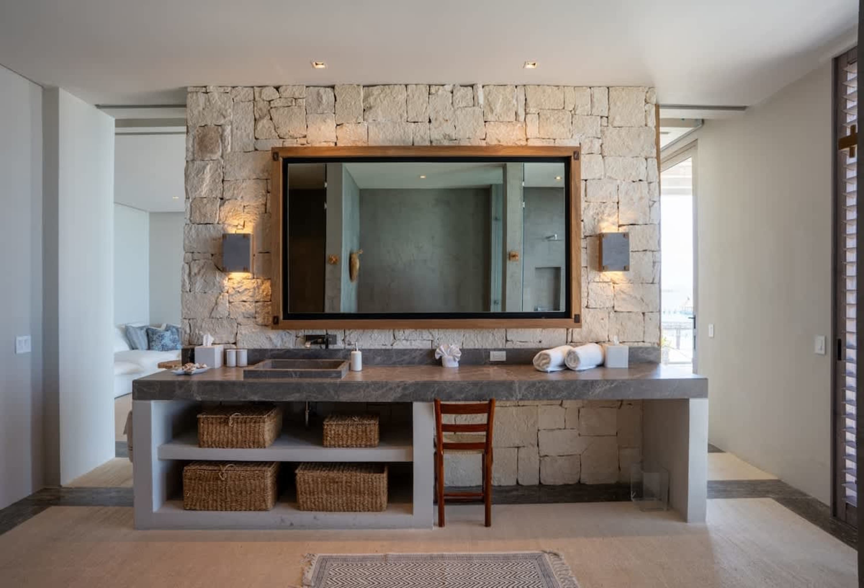 A large bathroom vanity with stone walls, a mirror, and storage baskets.