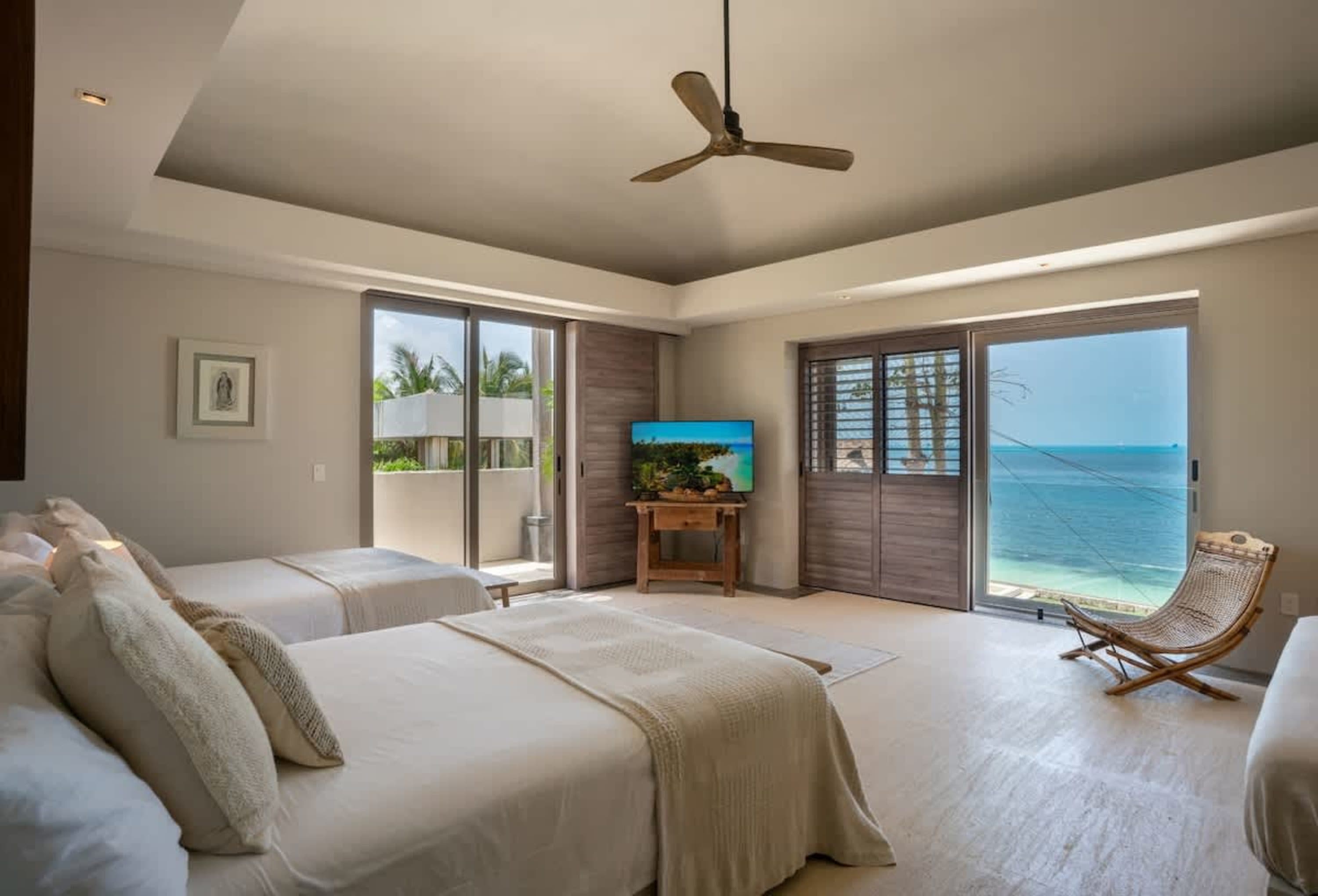 Bedroom with two beds, a TV, and a balcony overlooking the ocean.