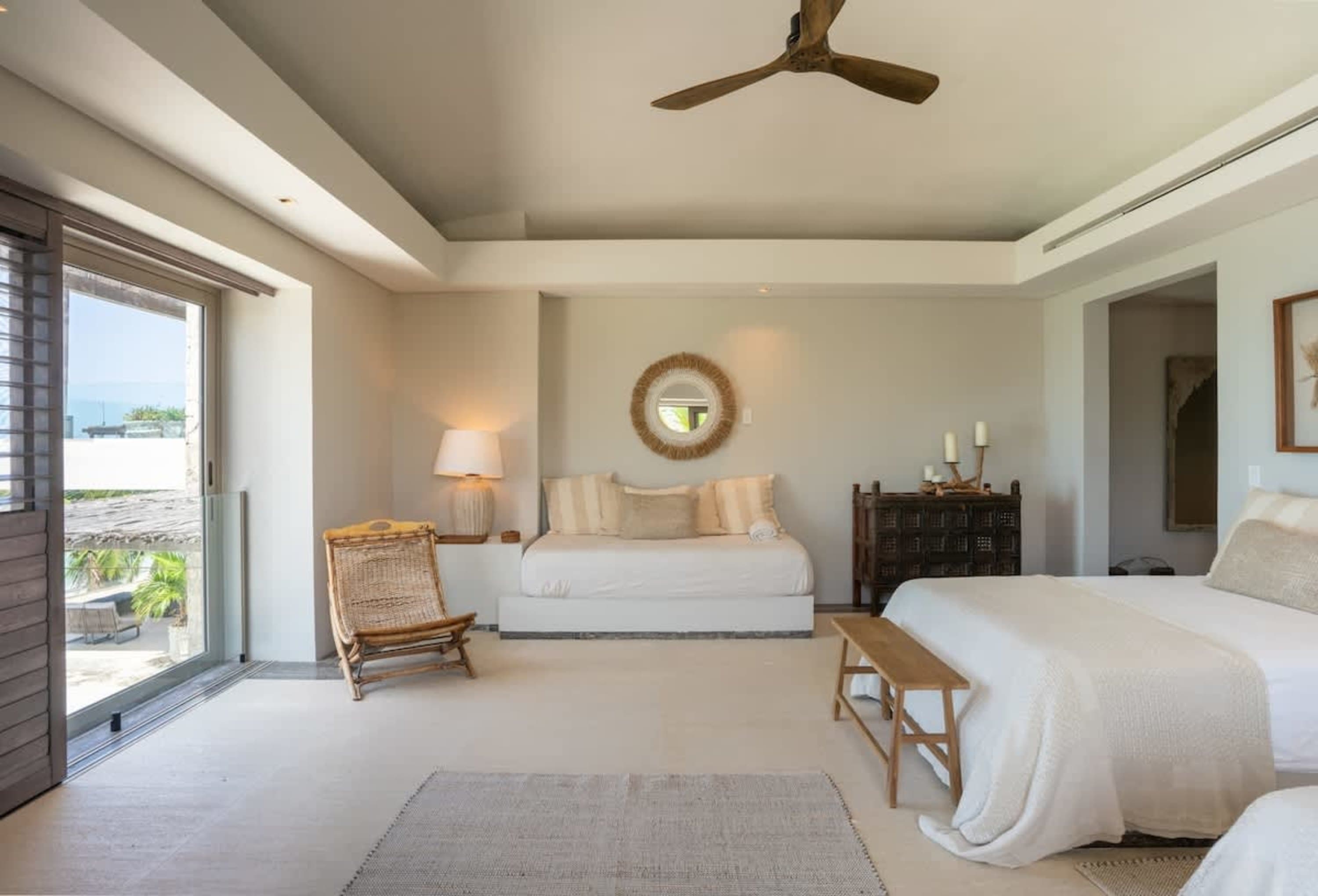 A bedroom with a white bed, a daybed, and a rattan chair.