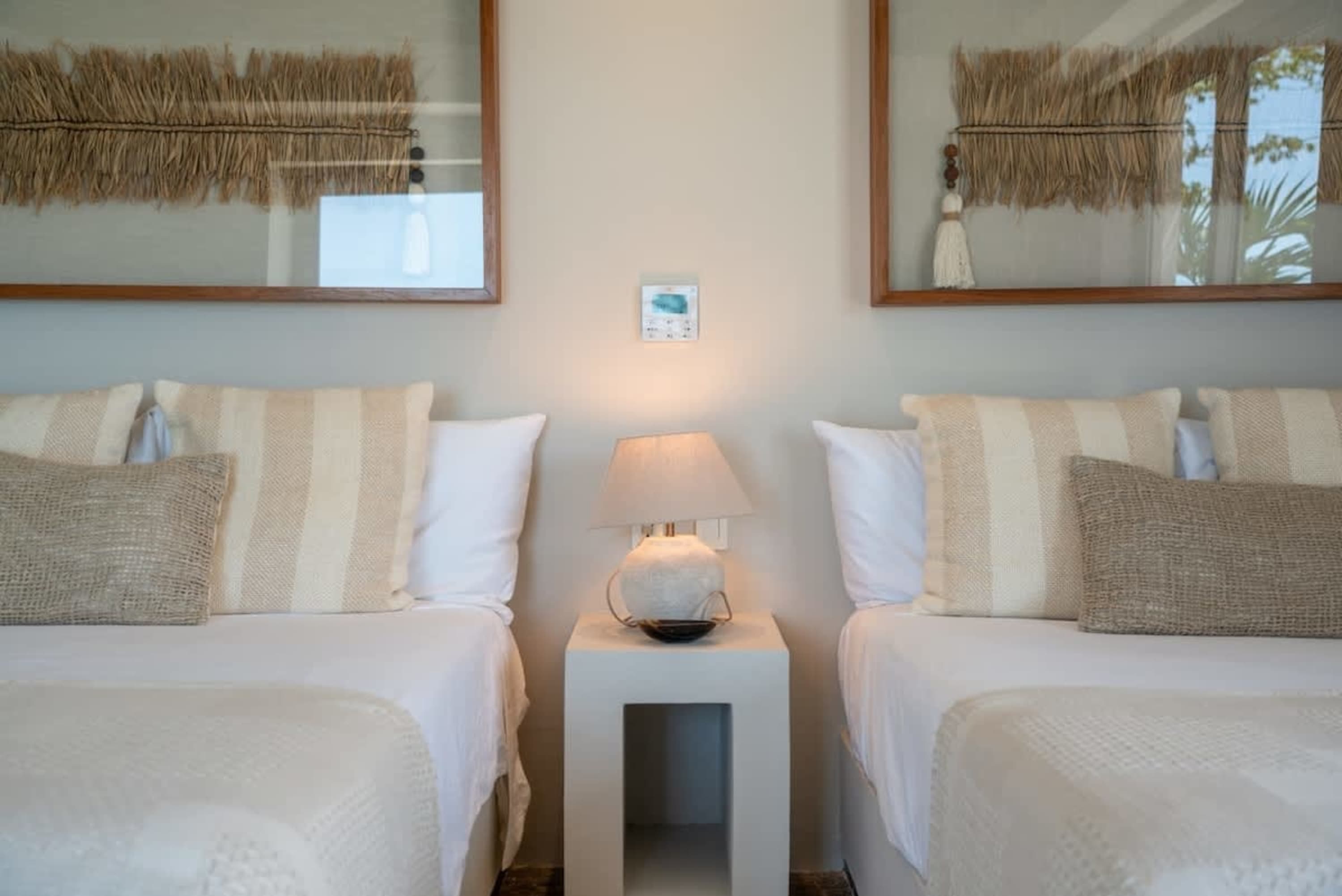 Two beds with white linens, striped and textured pillows, and framed artwork above.