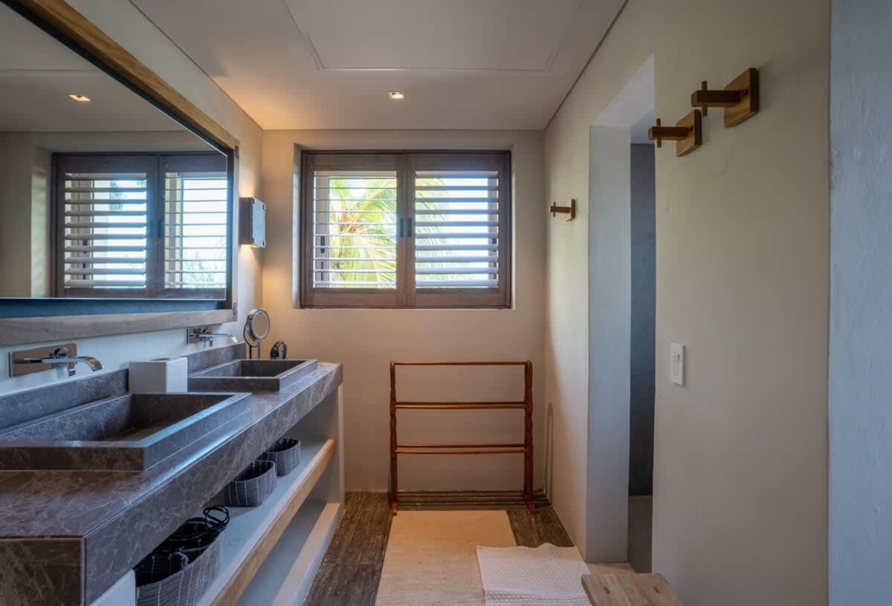 Bathroom with double vanity, window with shutters, and wooden towel rack.