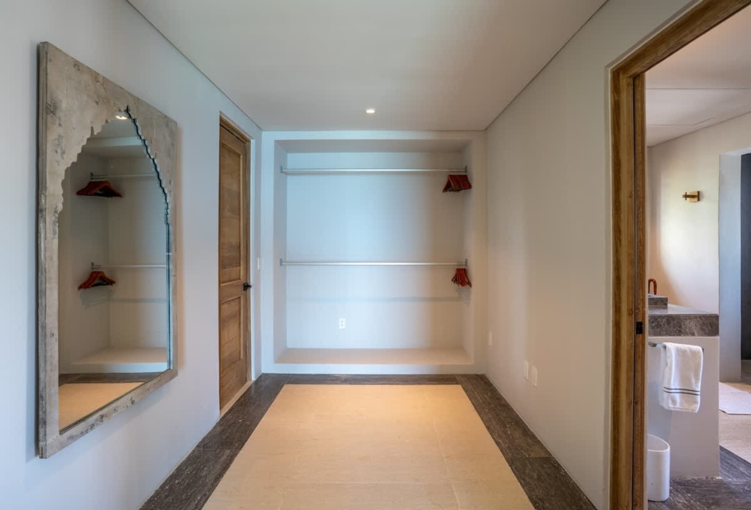 A hallway with a mirror, closet, and a door to a bathroom.