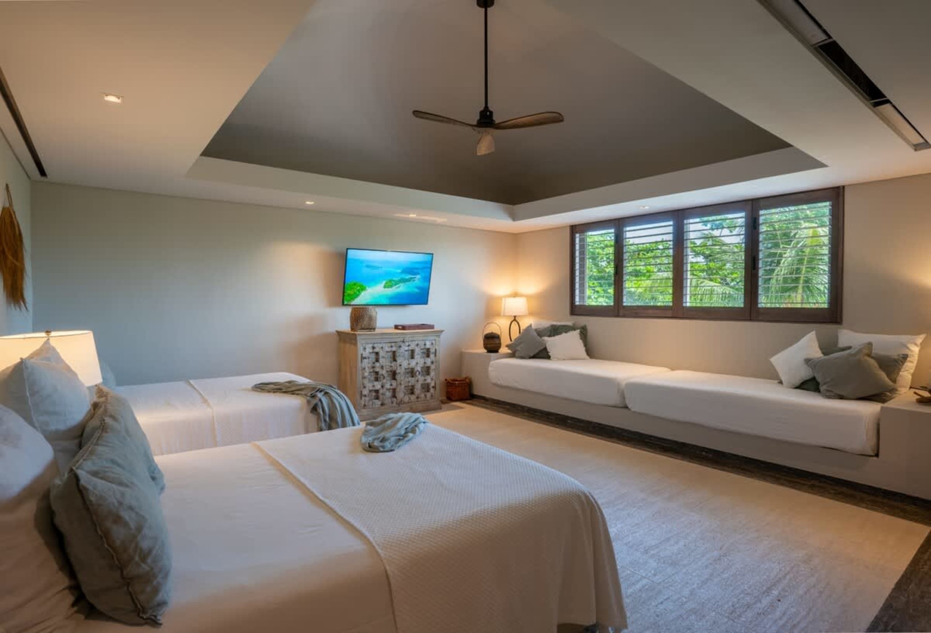 A bedroom with two beds, a long couch, and a tv.