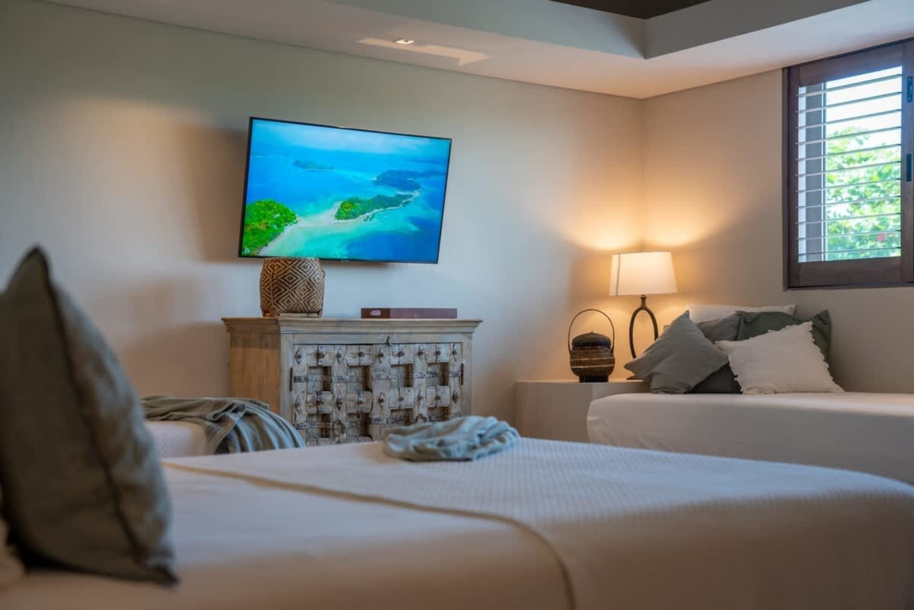 A bedroom with two beds, a TV, and a window with shutters.