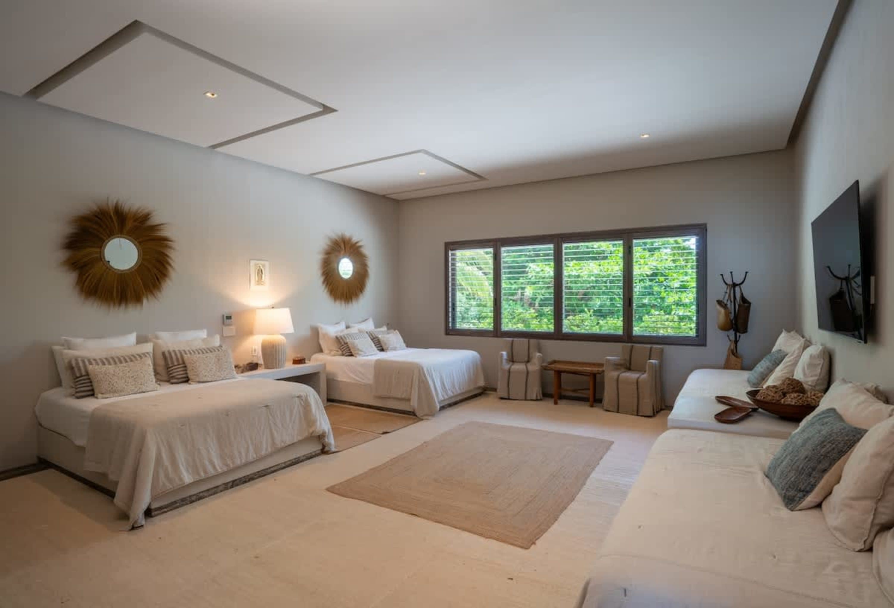 A spacious bedroom with two beds, two sofas, windows, and a TV.