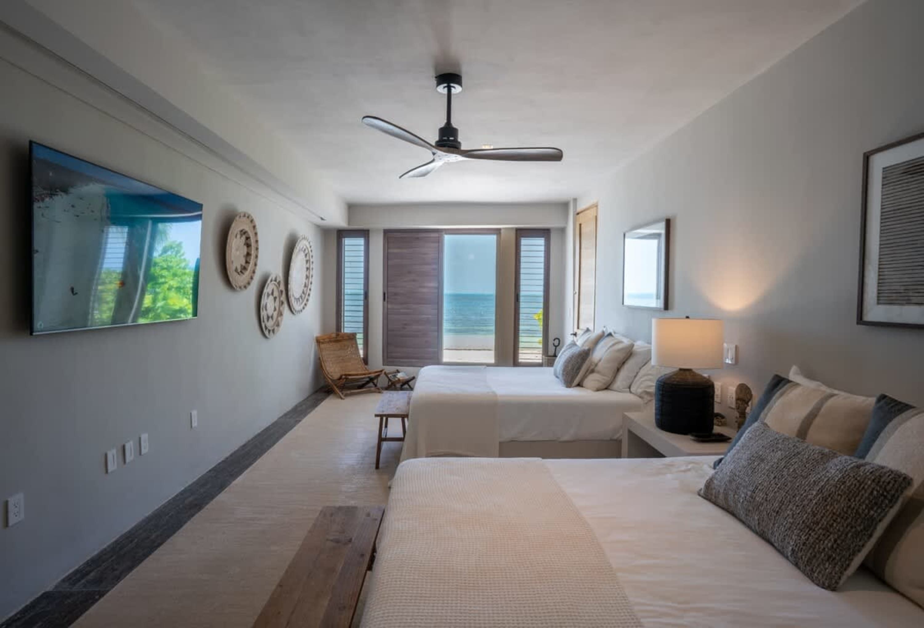 A bedroom with two beds, a TV, and a view of the ocean.