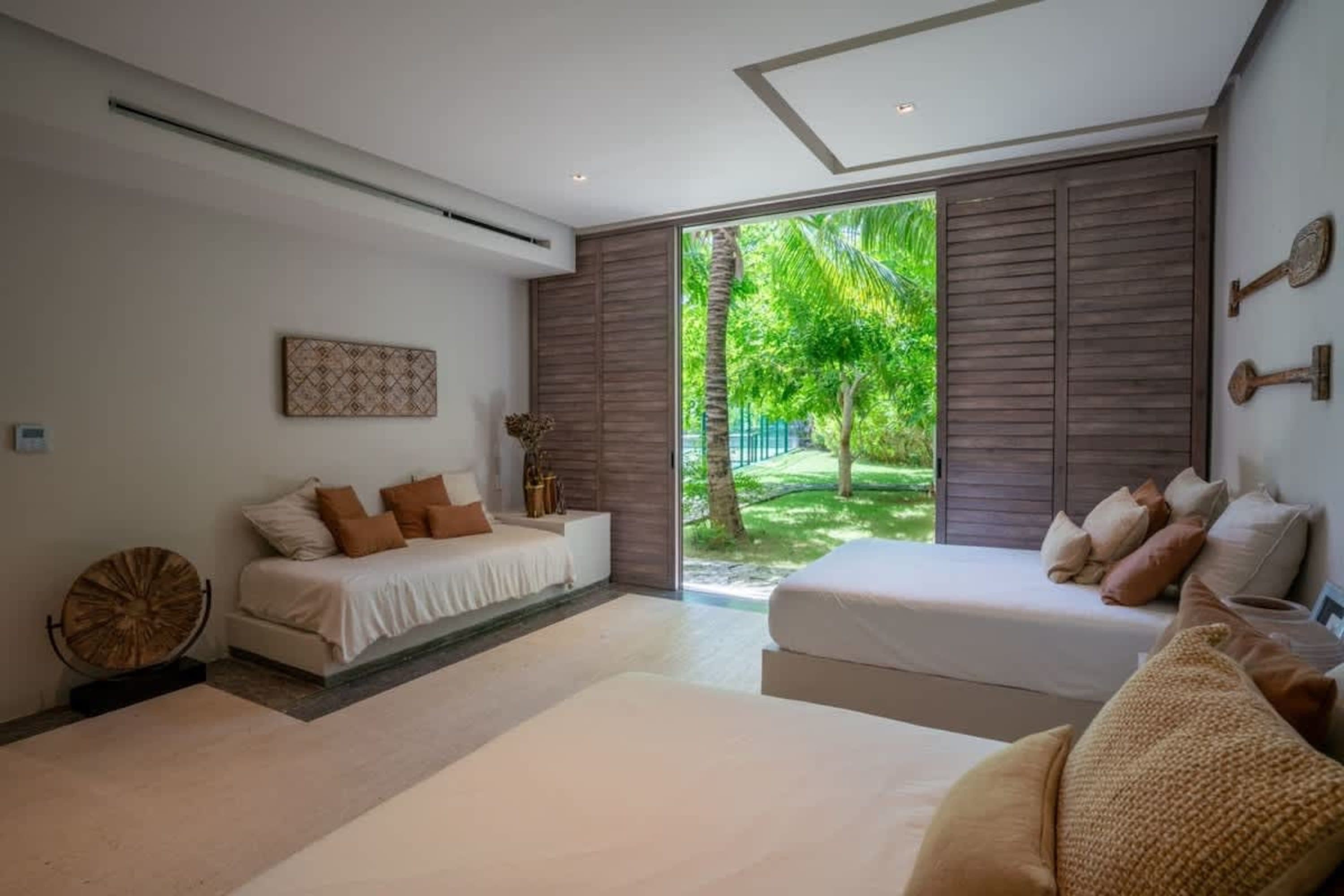 A bedroom with two beds and a view of a lush green garden.