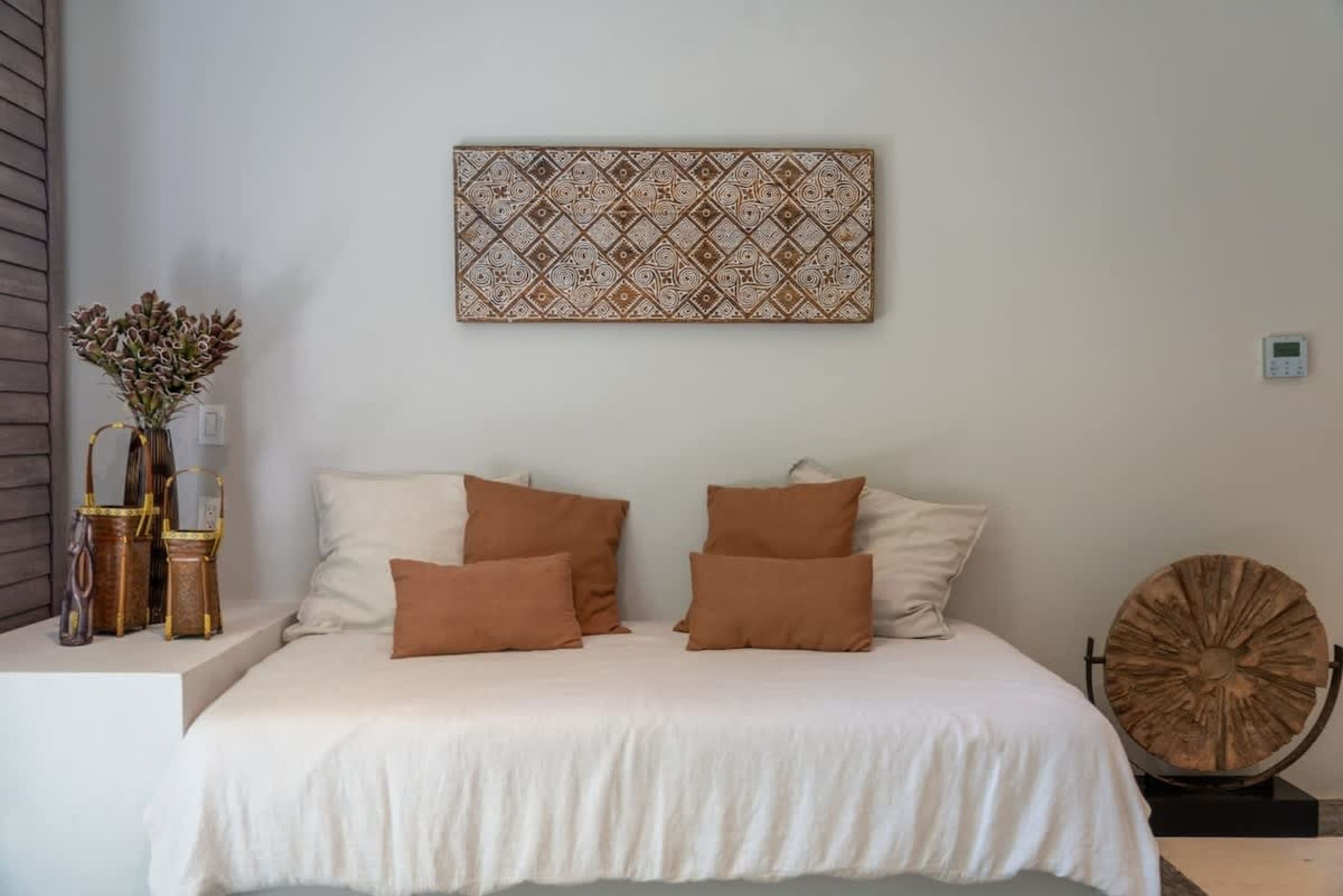 A minimalist bedroom with a white bed, brown pillows, and wooden wall art.