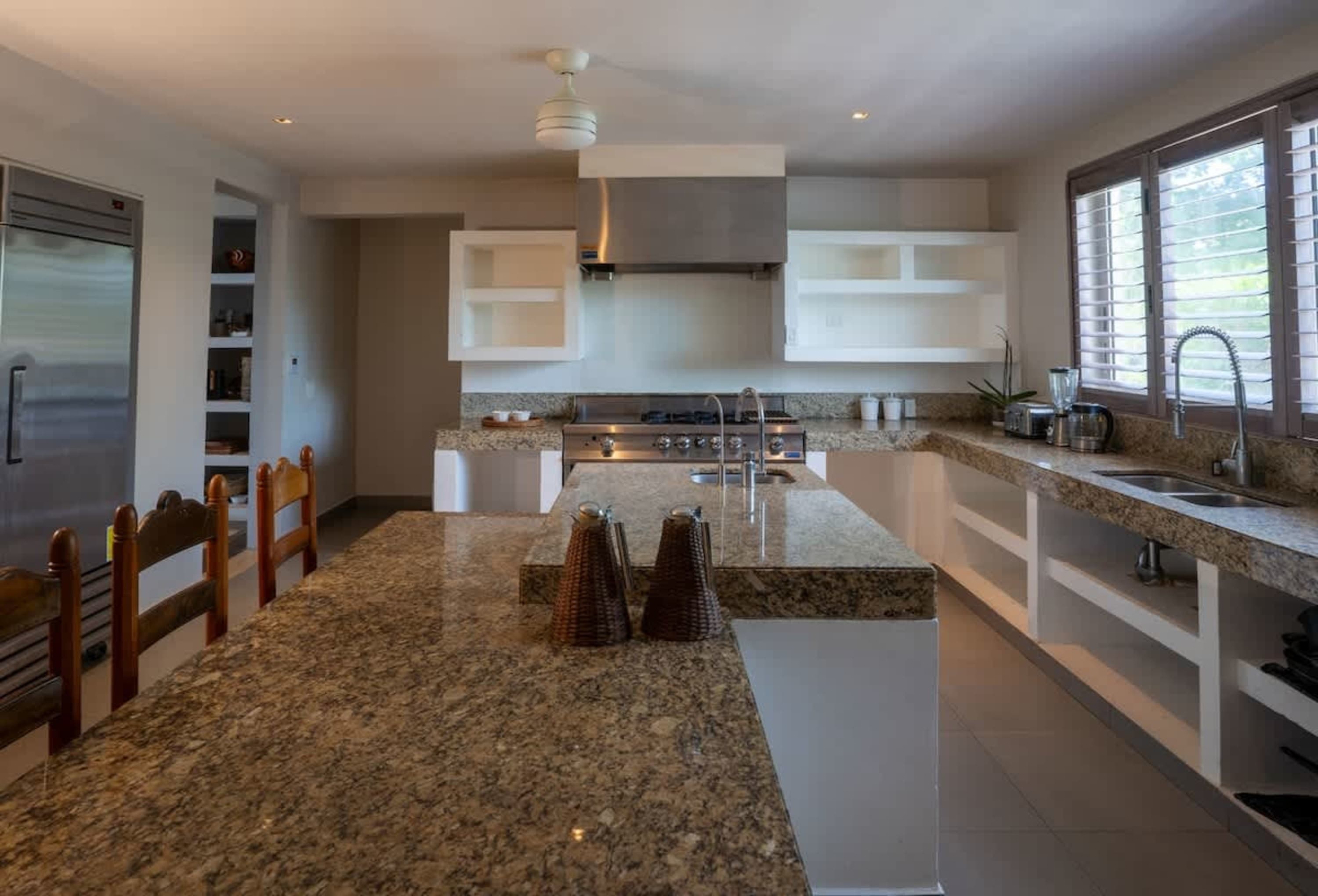 A modern kitchen with granite countertops, stainless steel appliances, and wooden chairs.
