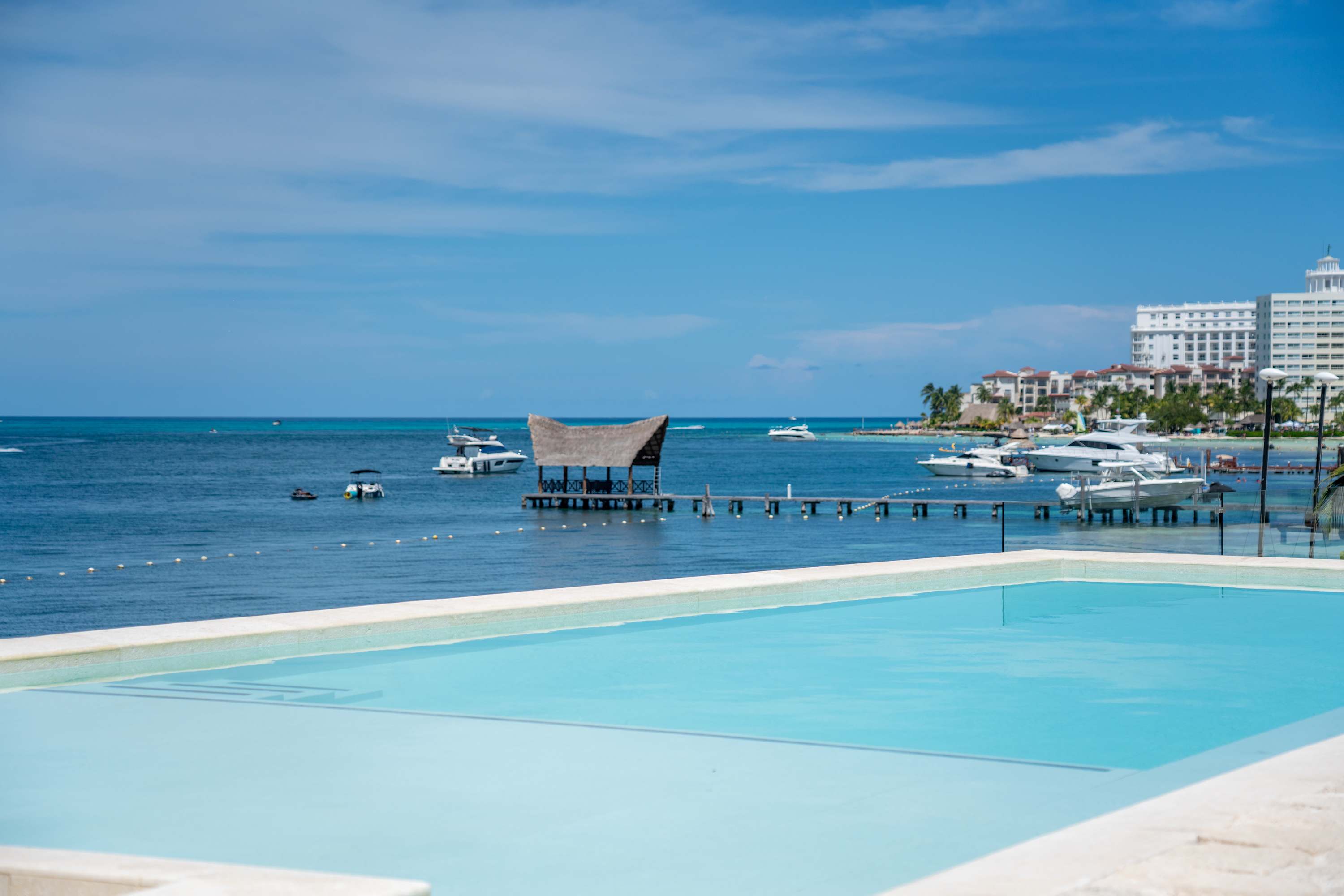 A resort with a pool, yachts, and buildings on a sunny day.