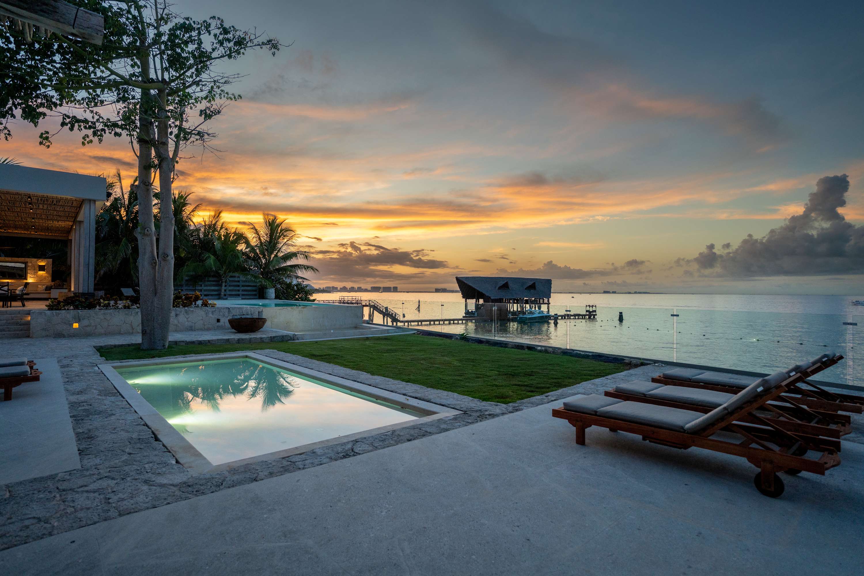 A serene beach resort at sunset with infinity pools, lounge chairs, and a thatched-roof cabana.