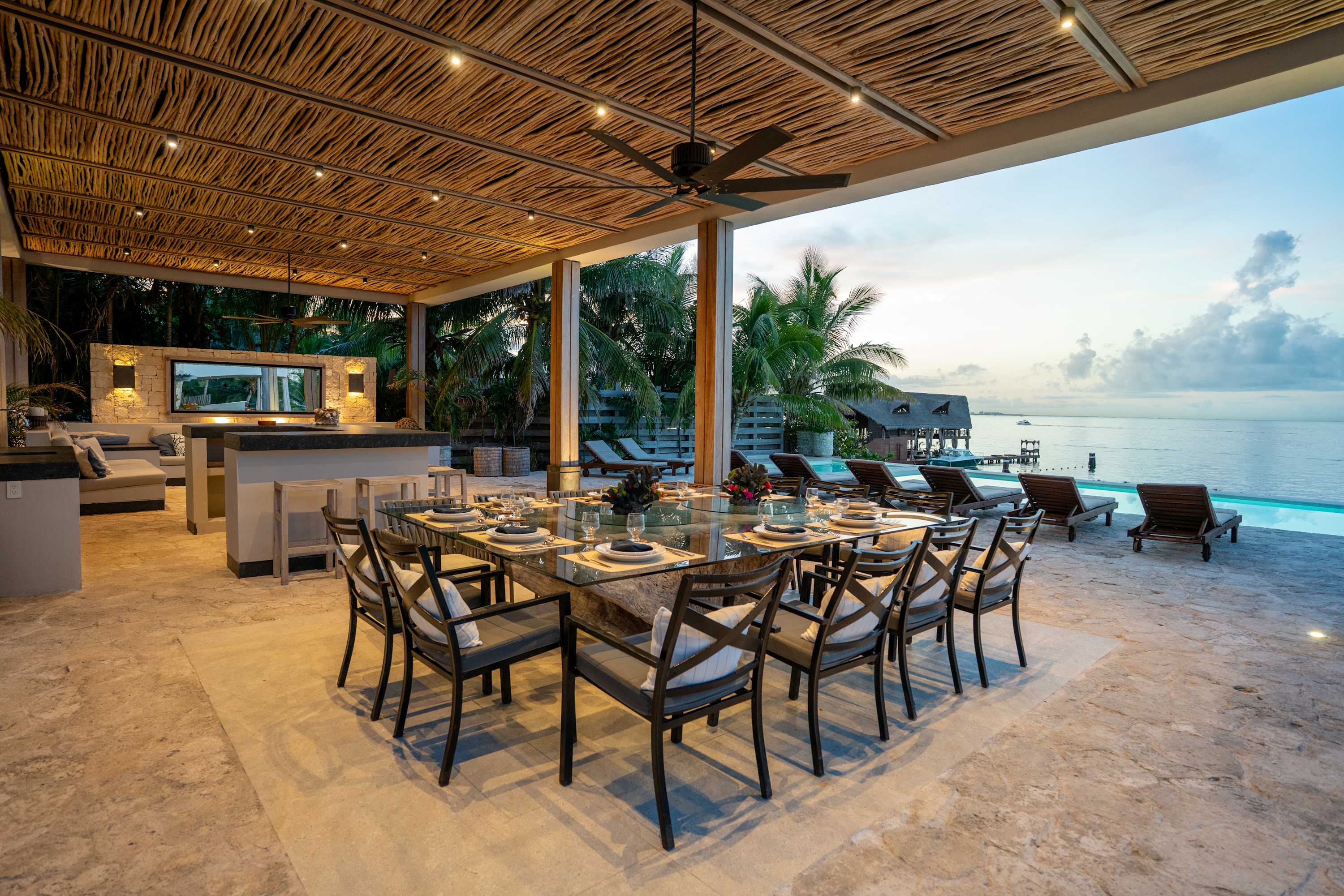 Outdoor dining area with a glass table, chairs, bar, and ocean view.
