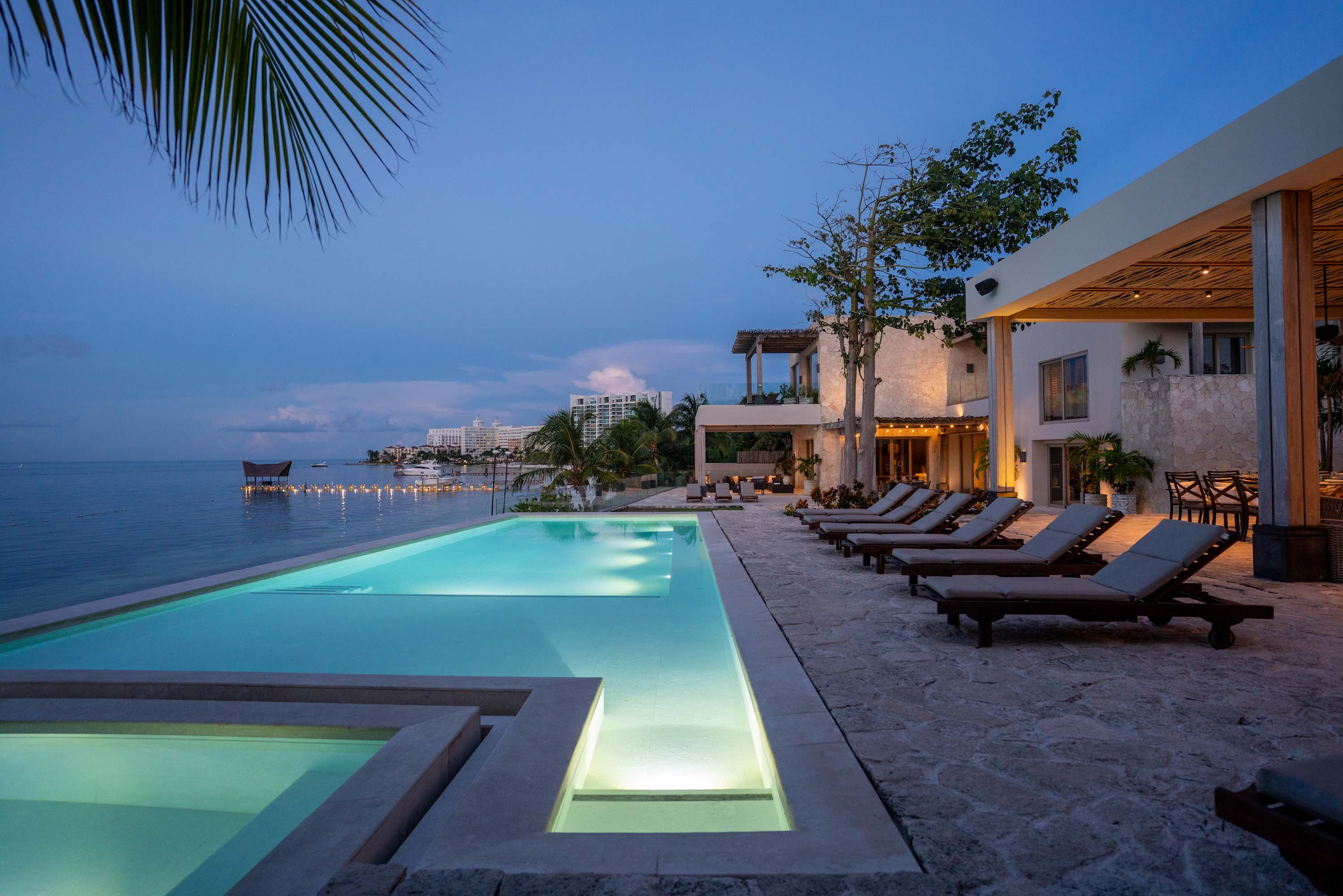 Infinity pool overlooking the ocean at dusk, with lounge chairs and a modern villa.