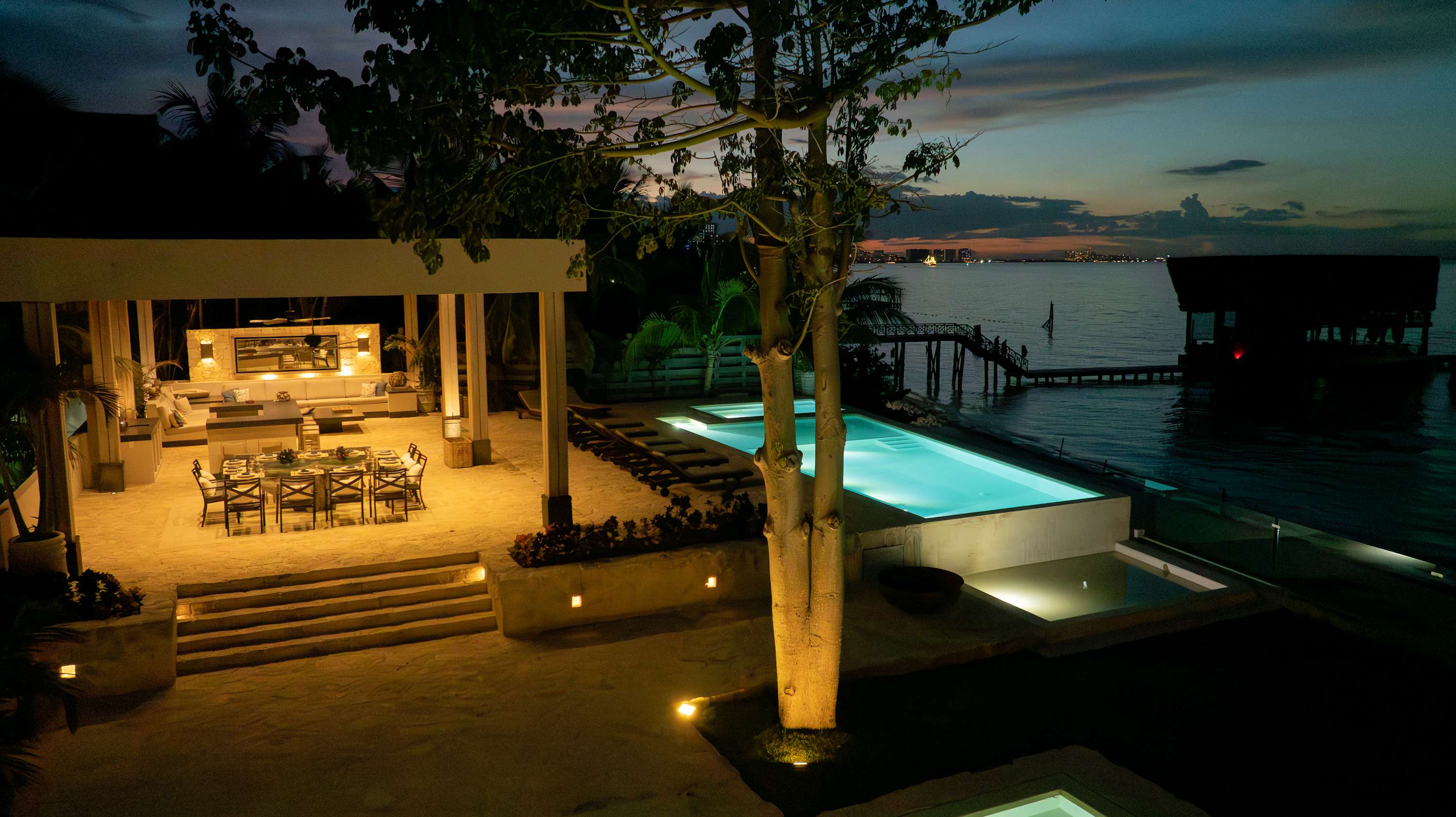 A luxurious nighttime view of a resort with a pool and dining area overlooking the ocean.
