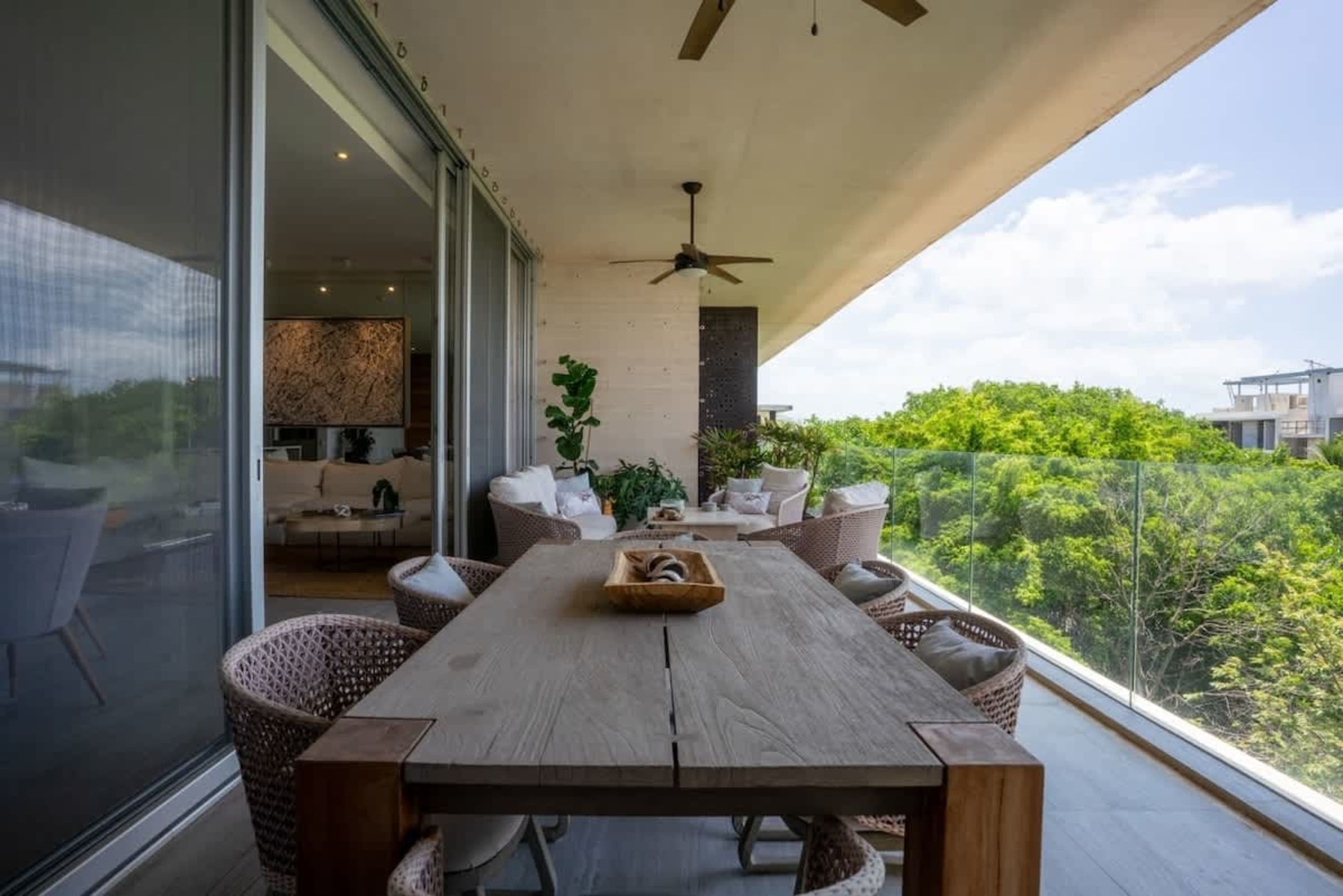 Outdoor dining area with a wooden table and chairs on a balcony overlooking lush greenery.