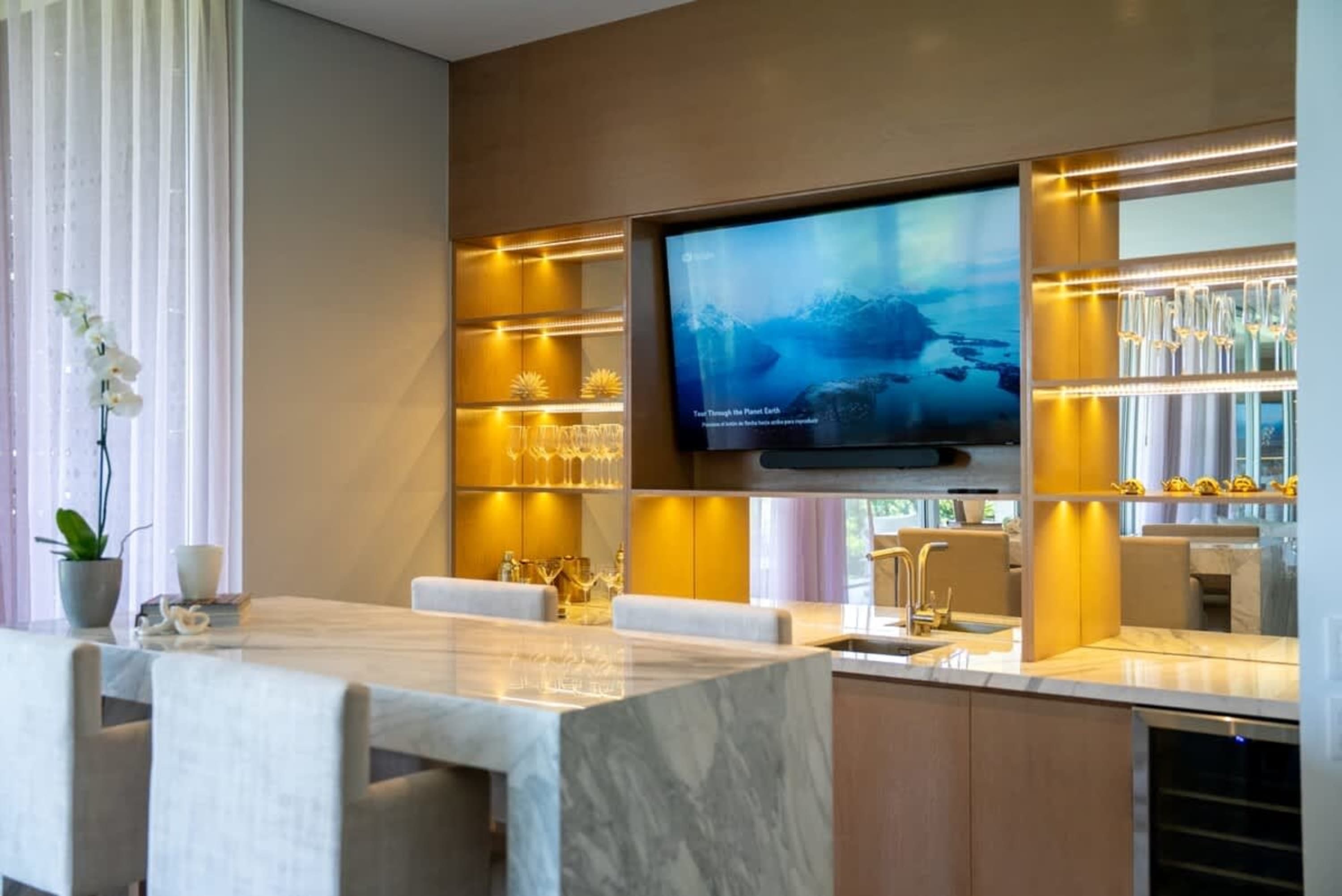 A modern bar area with a marble countertop, built-in shelves, and a TV.