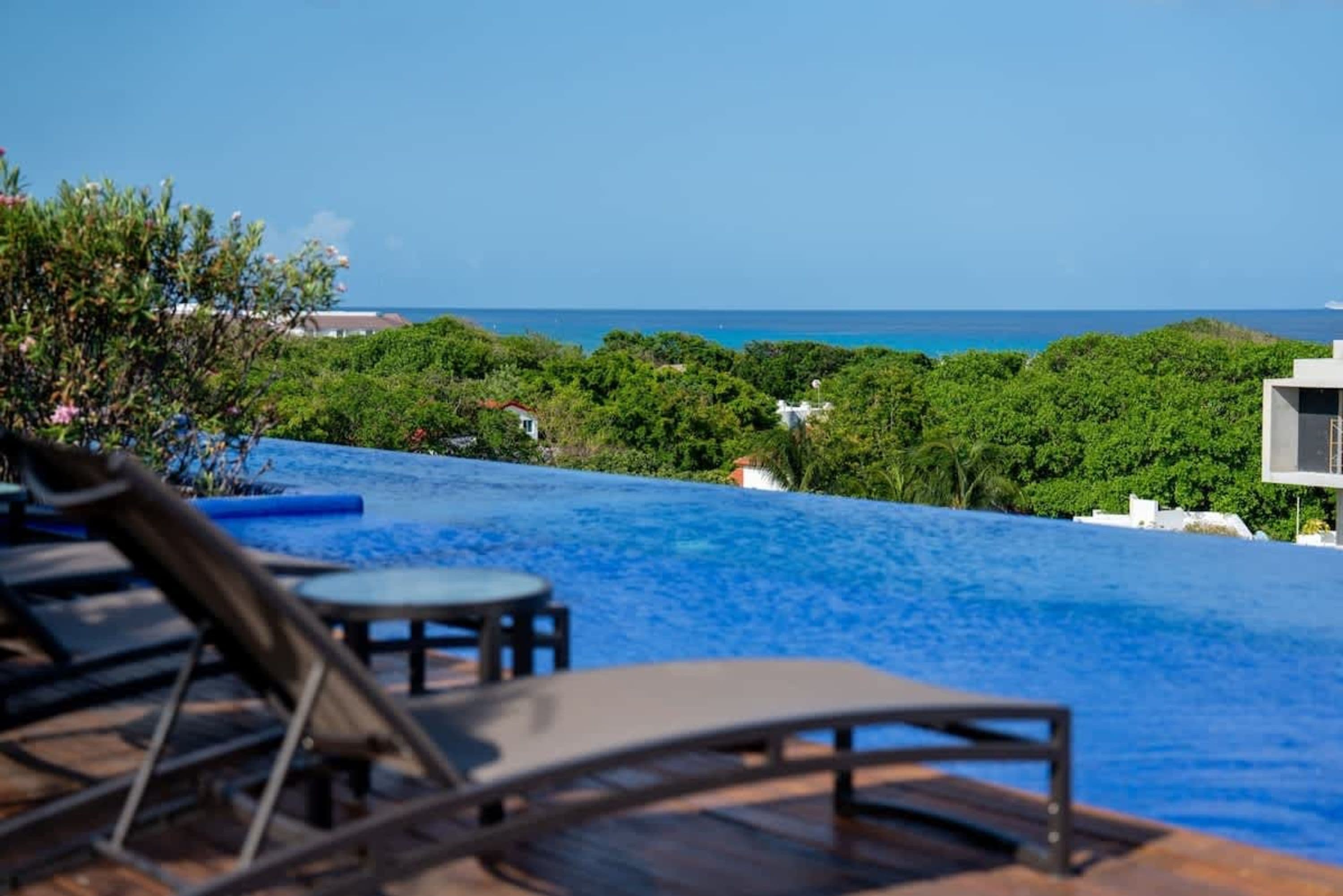 Infinity pool with lounge chairs overlooks lush green trees and the ocean.