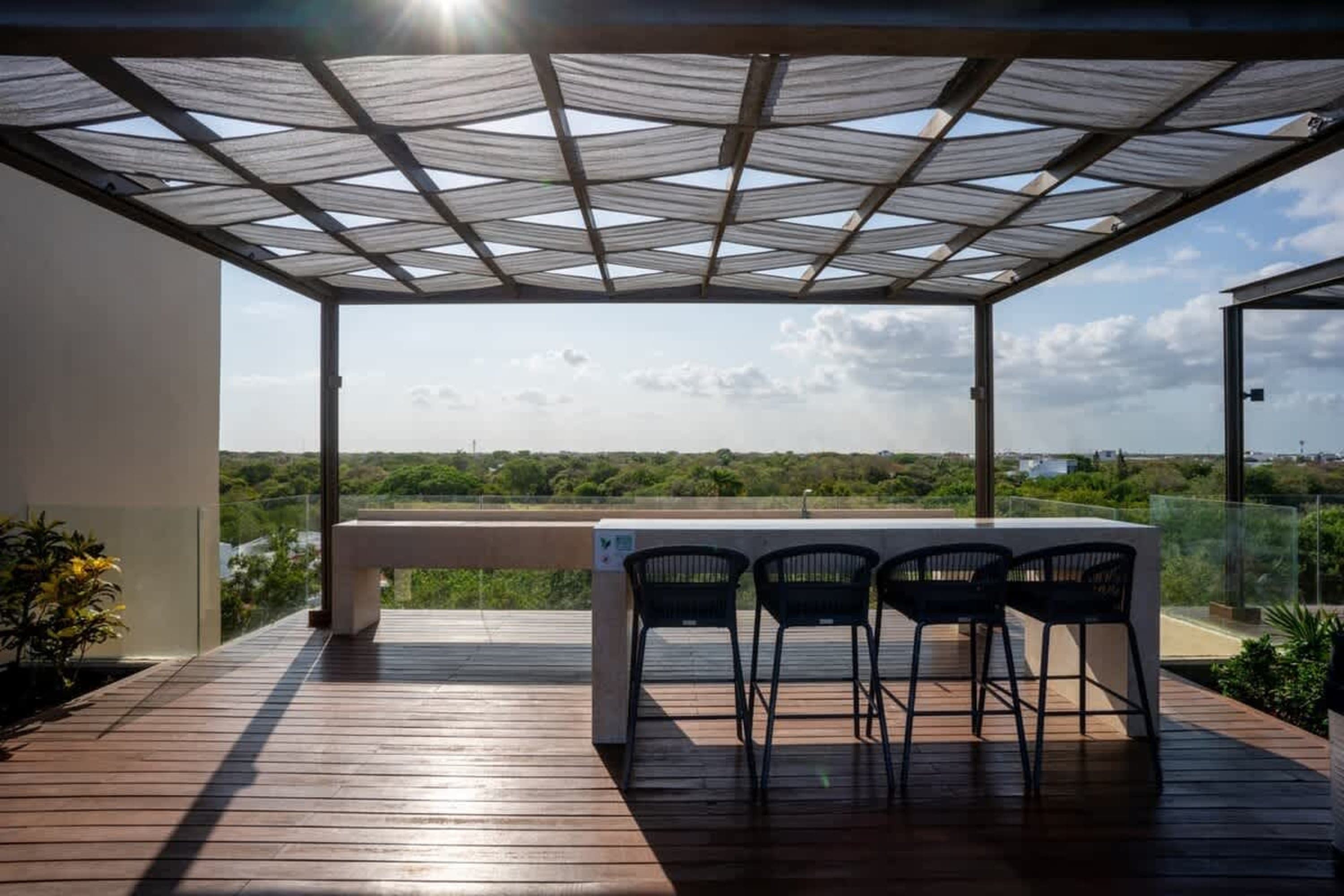 Outdoor bar and seating area with a view of lush greenery under a shaded pergola.