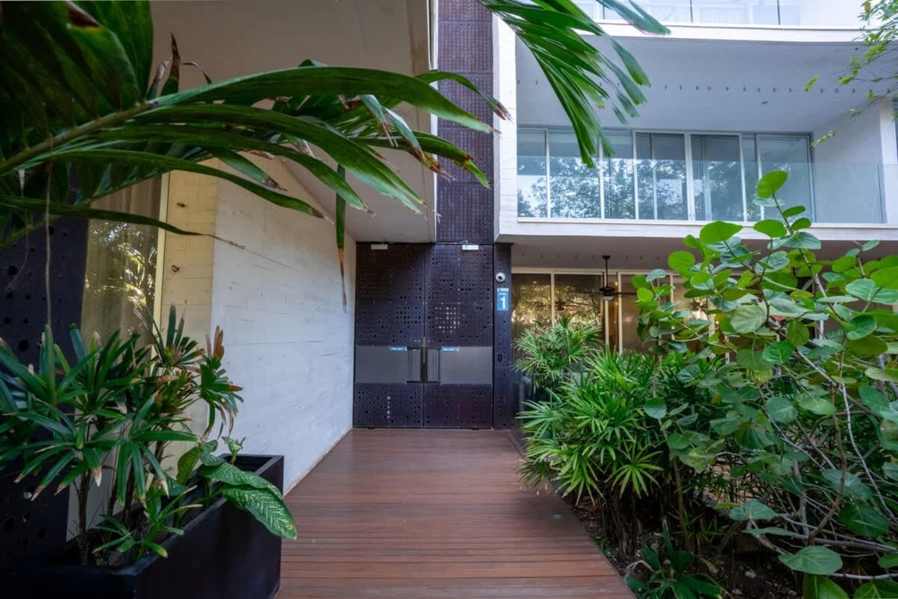 Modern building entrance with wooden walkway and lush greenery.