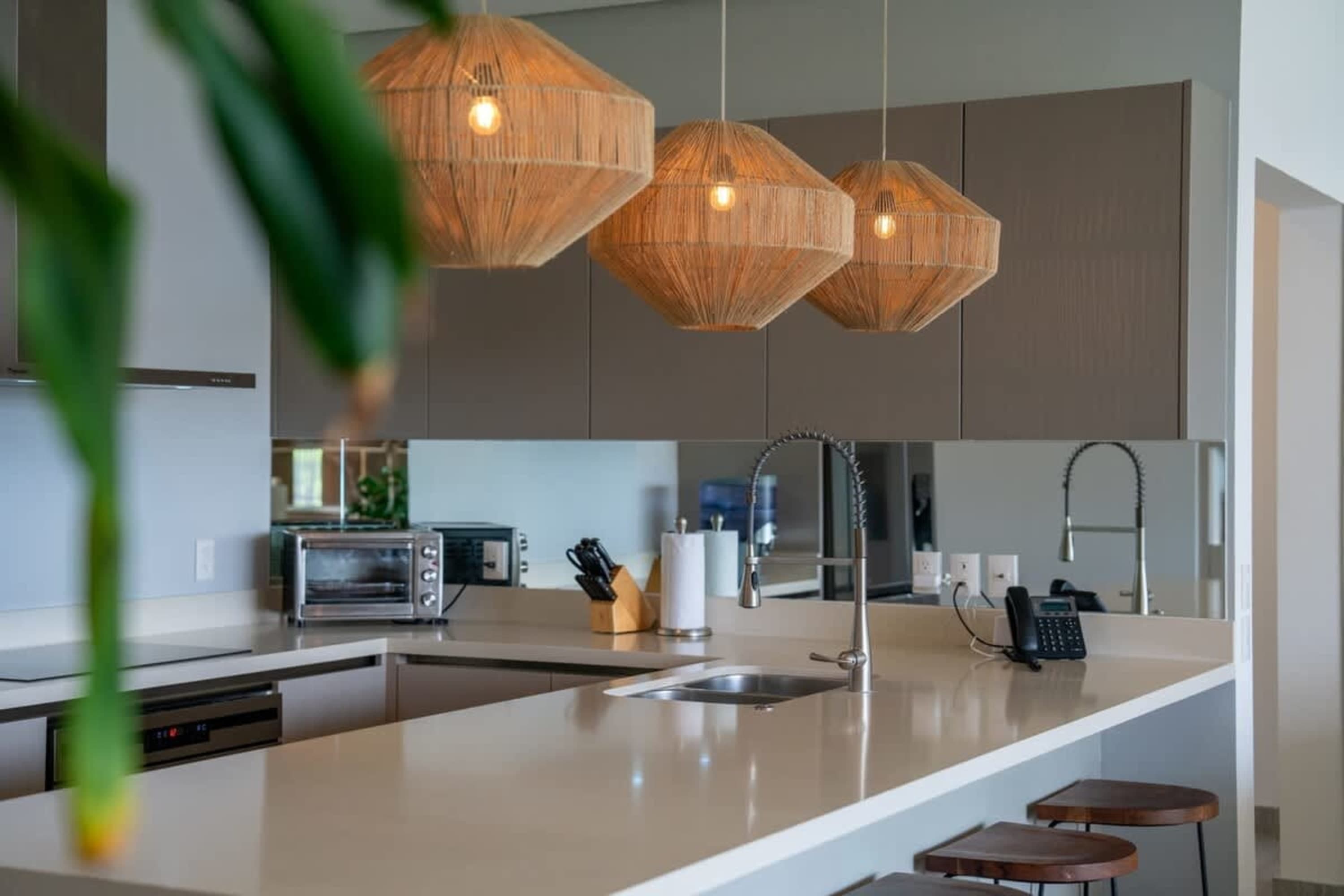 A modern kitchen island with three woven pendant lights and a stainless steel sink.
