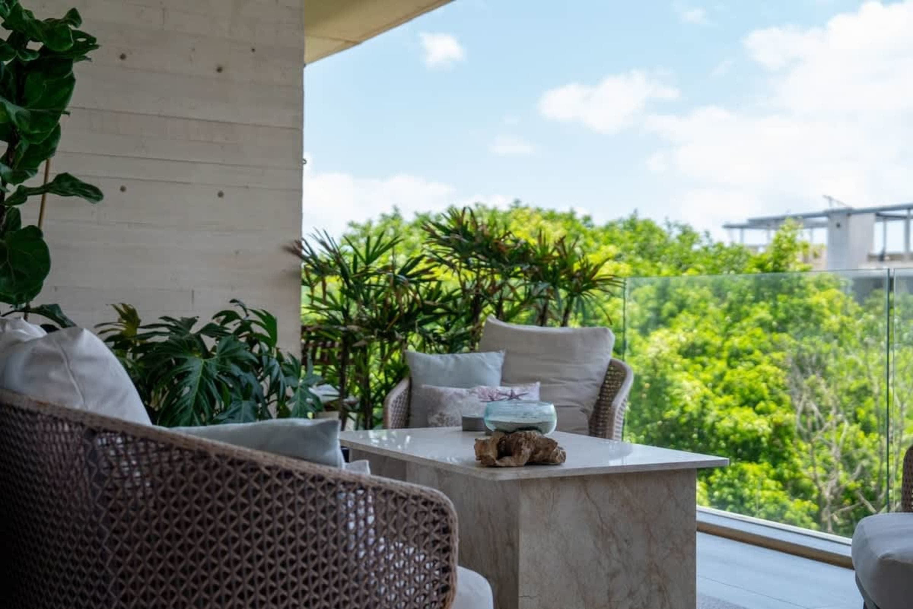 A patio with woven chairs and a marble table overlooking lush green trees.