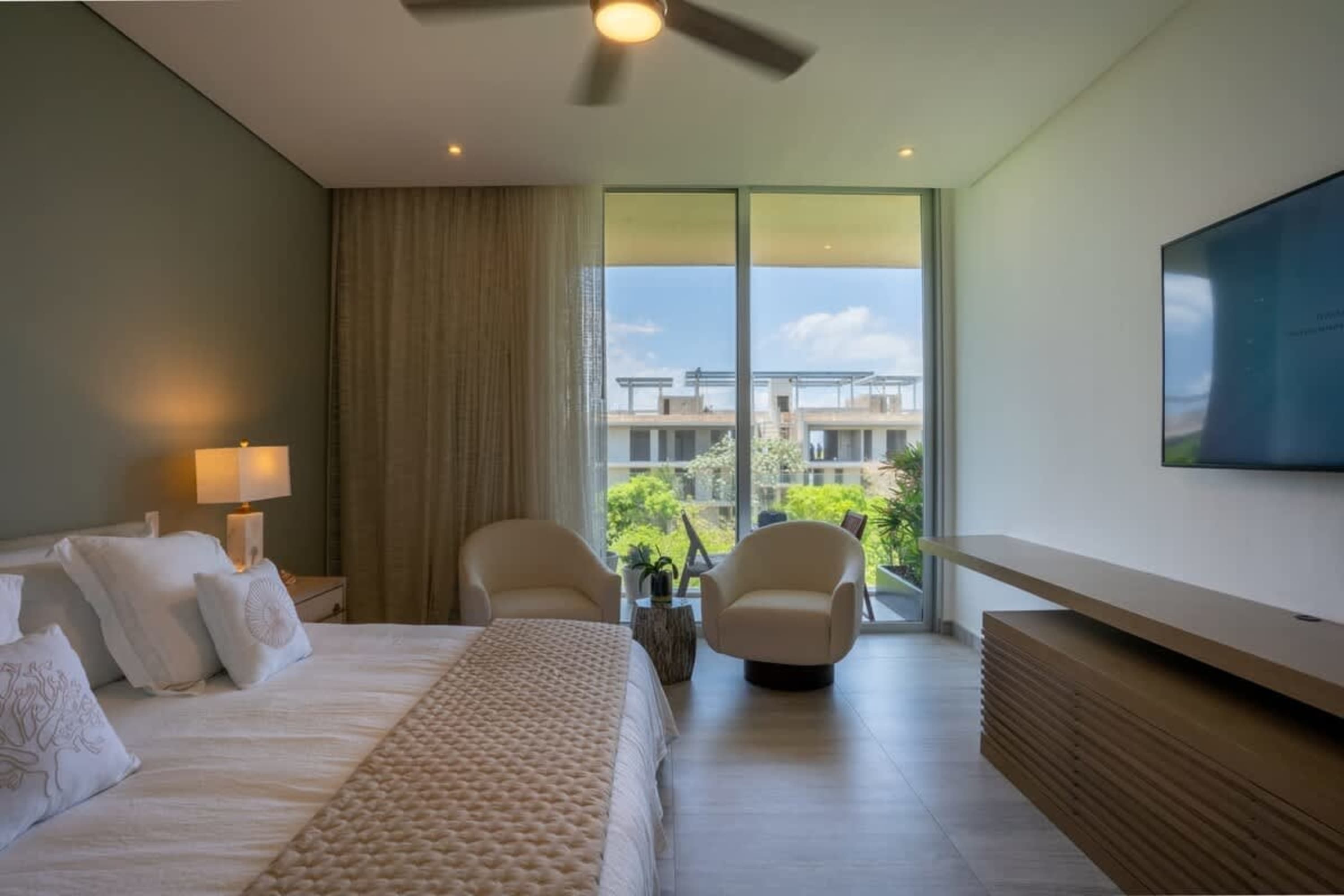 A spacious bedroom with a bed, two chairs, and a TV.