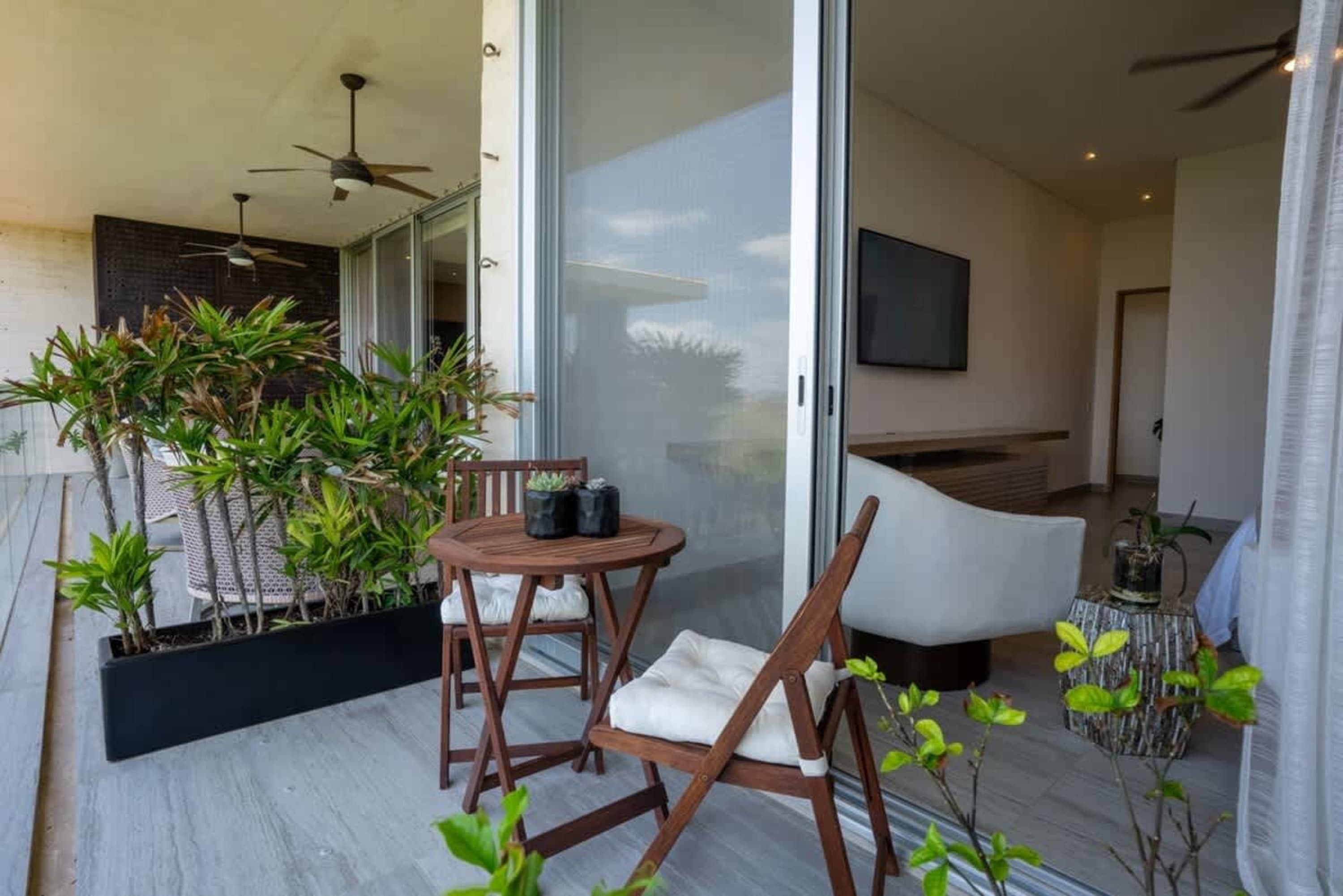A balcony with chairs and a table, overlooking a room with a TV.