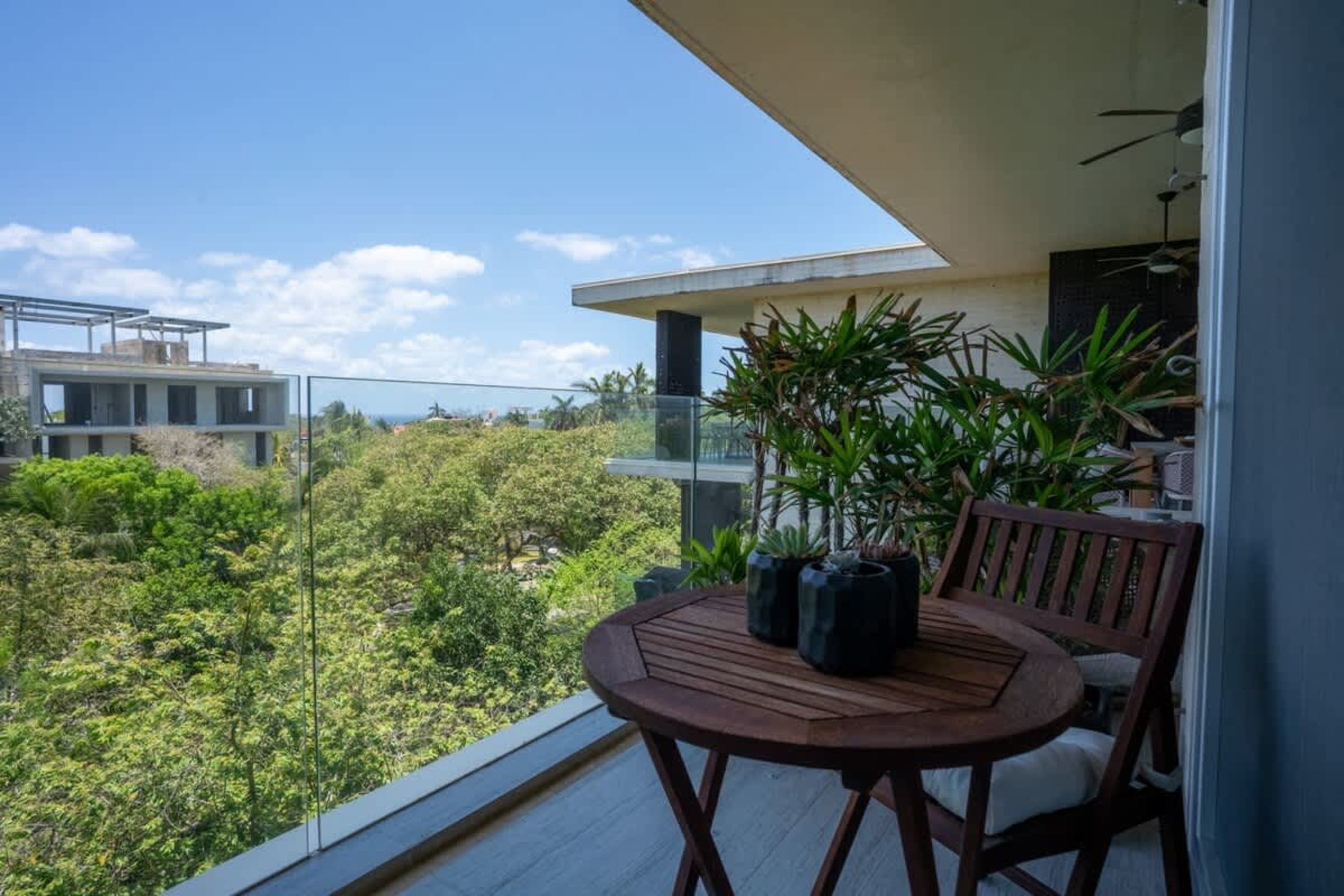A wooden table and chairs on a balcony overlooking lush greenery and a partially built structure.