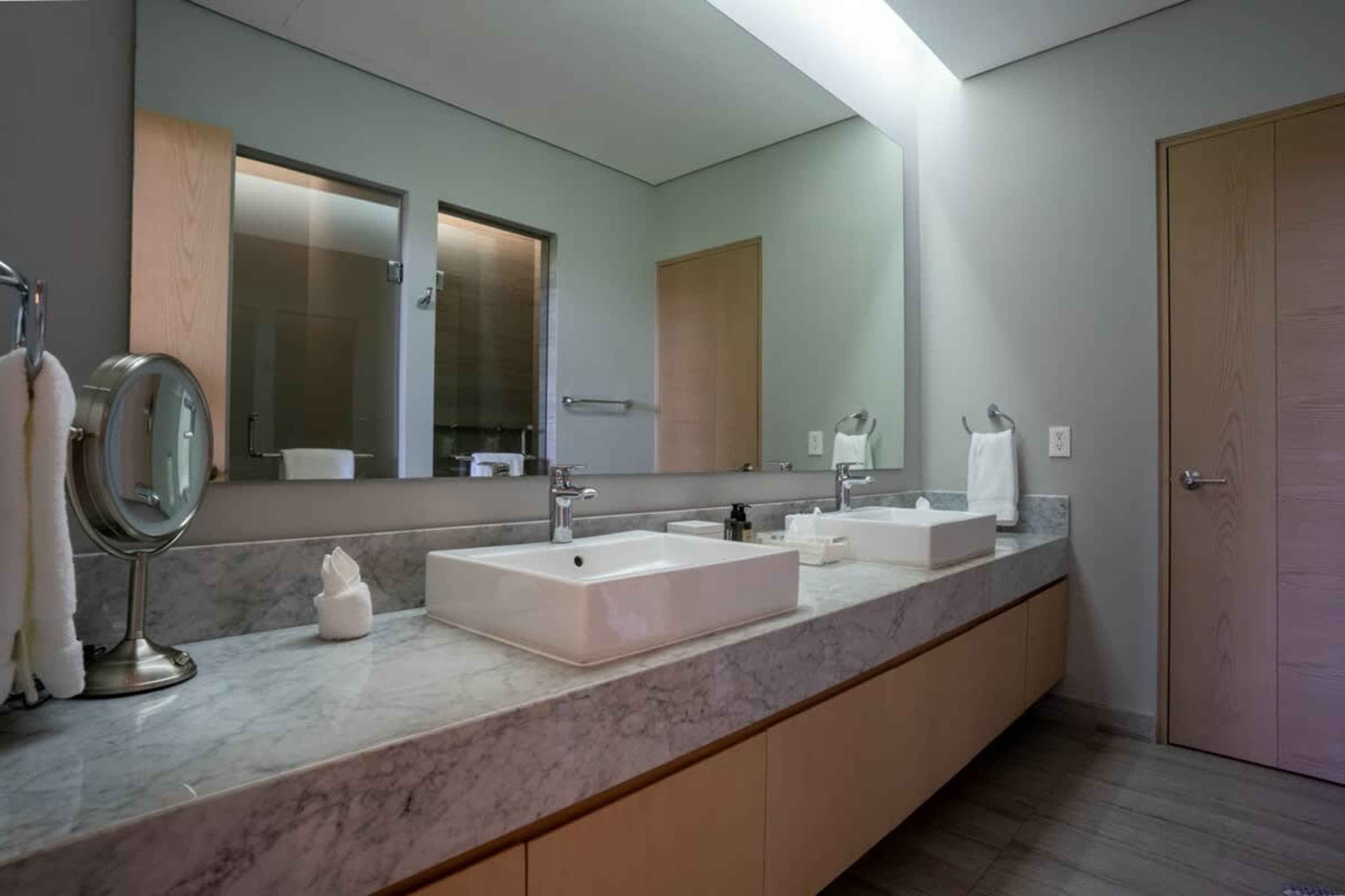 A modern bathroom vanity with two sinks, marble countertops, and a large mirror.