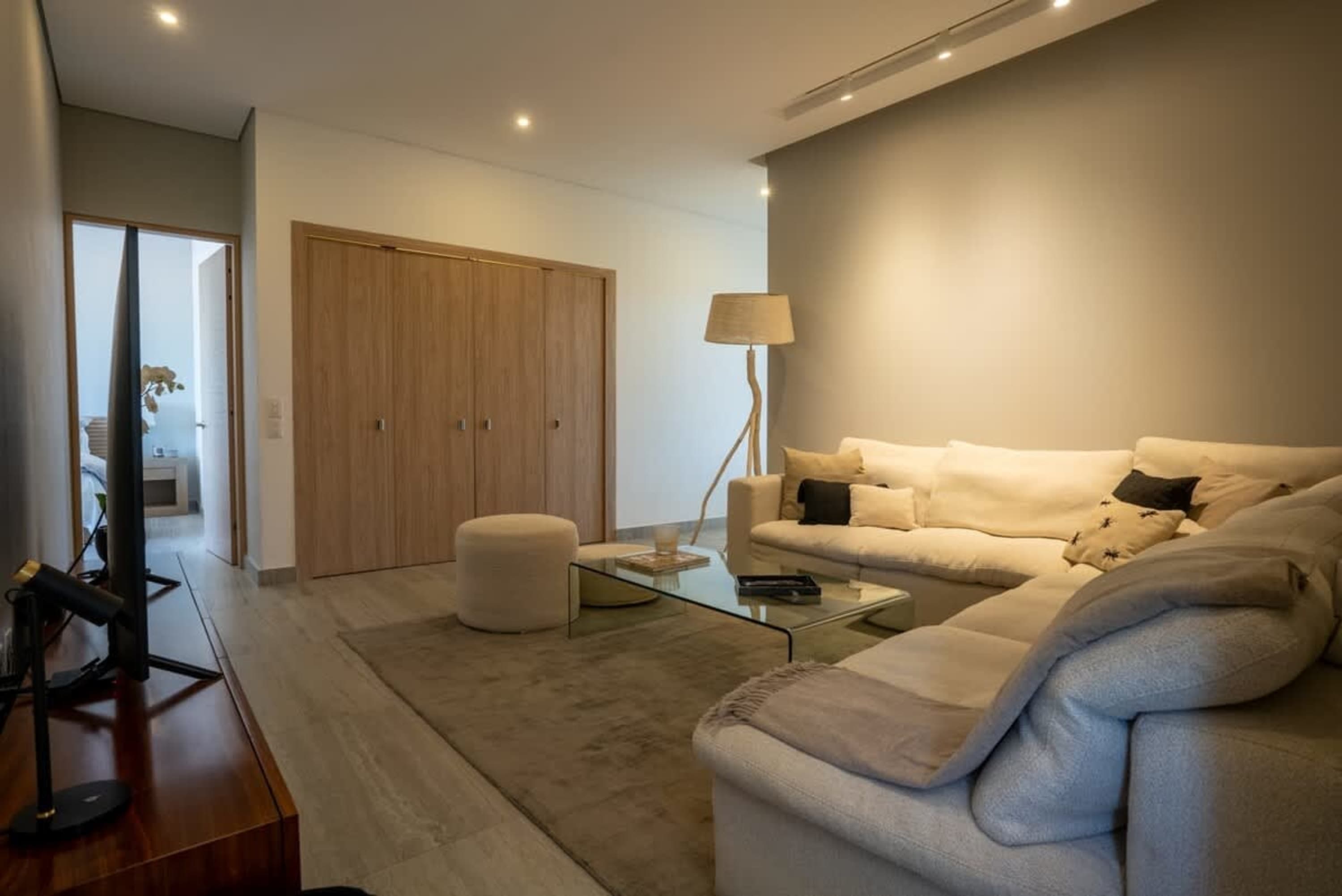 Modern living room with sectional couch, glass coffee table, and wooden closet doors.