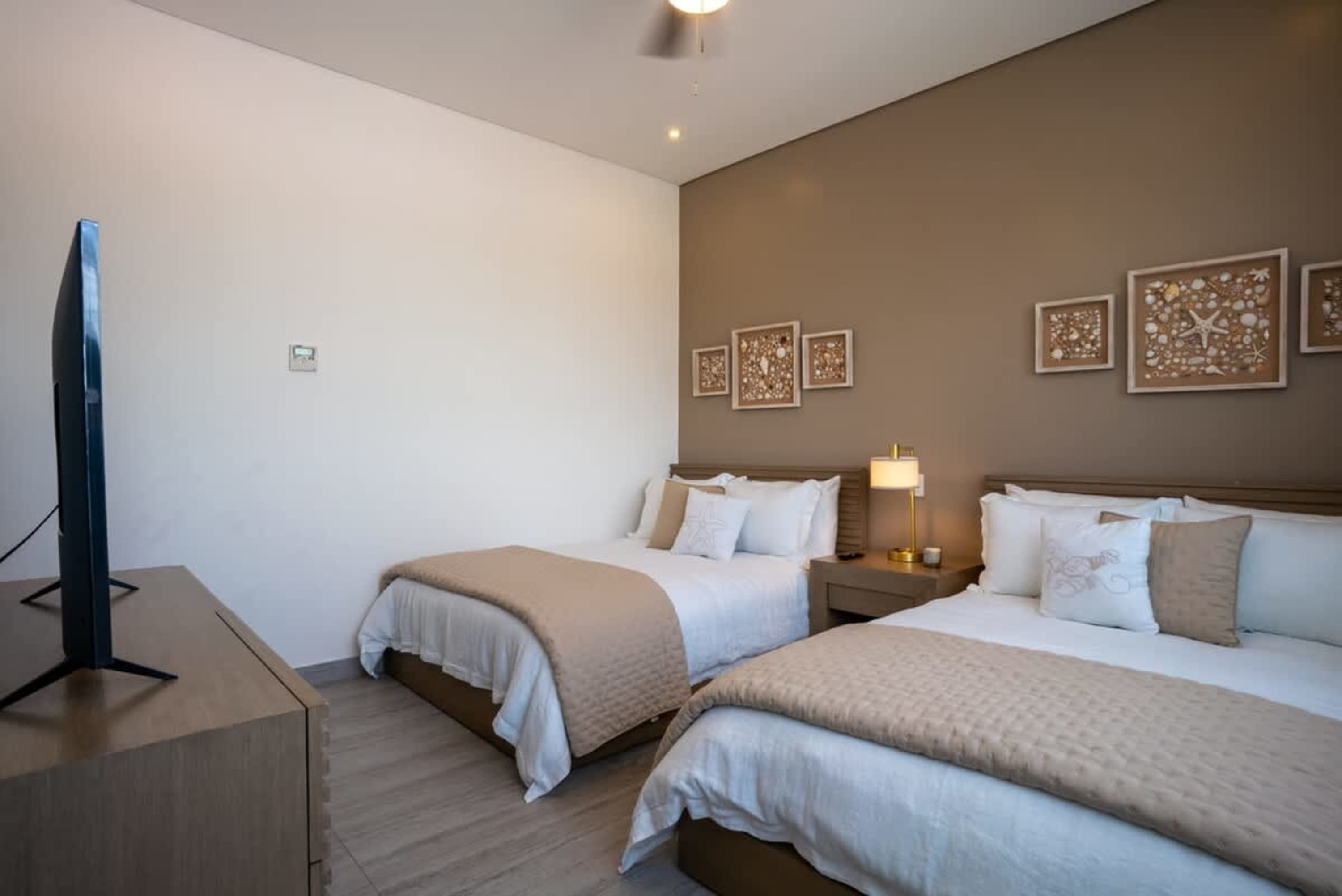 Bedroom with two beds, a TV, and seashell artwork on the wall.