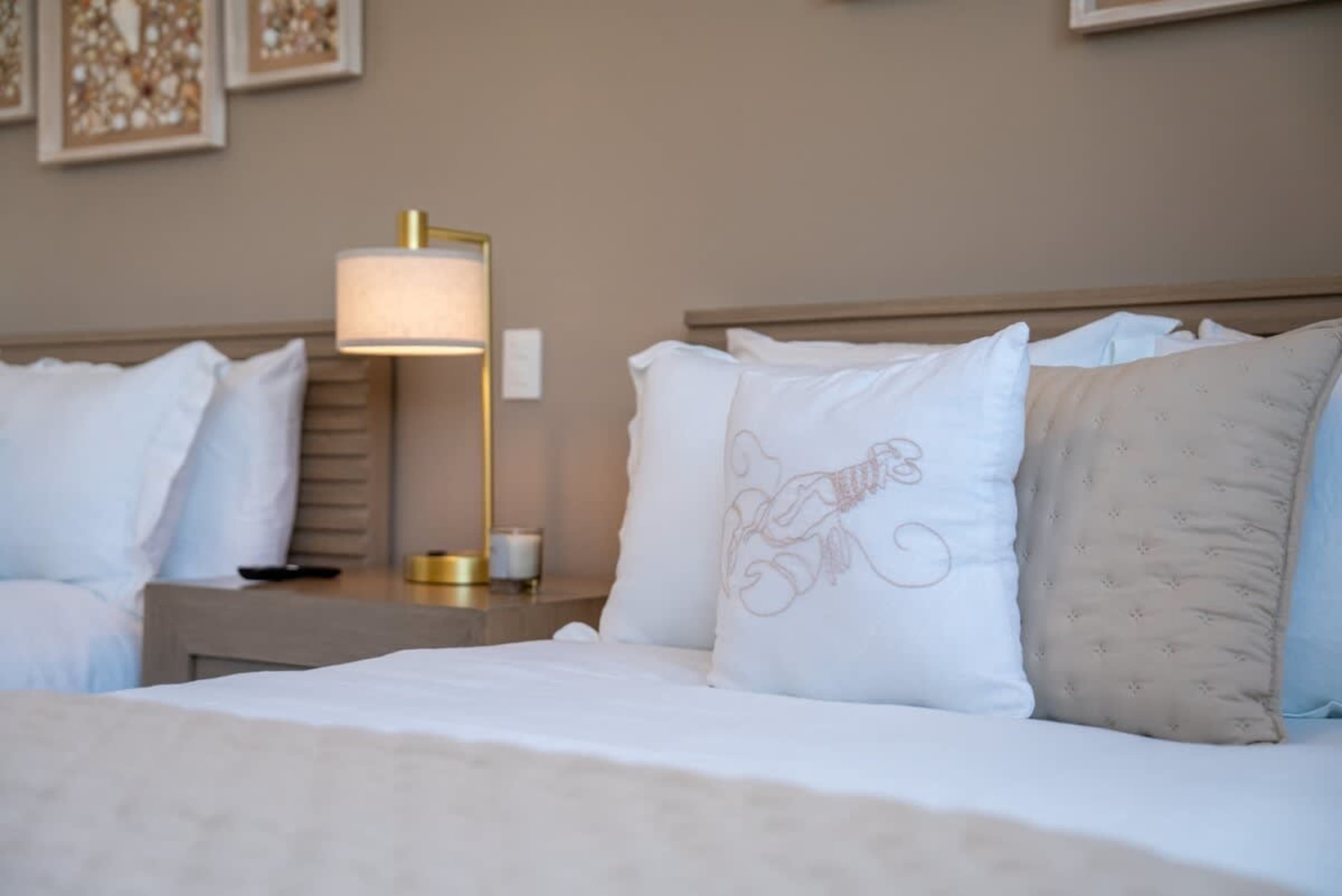 Two beds with white linens and pillows, one with a lobster design. A bedside lamp and framed art are