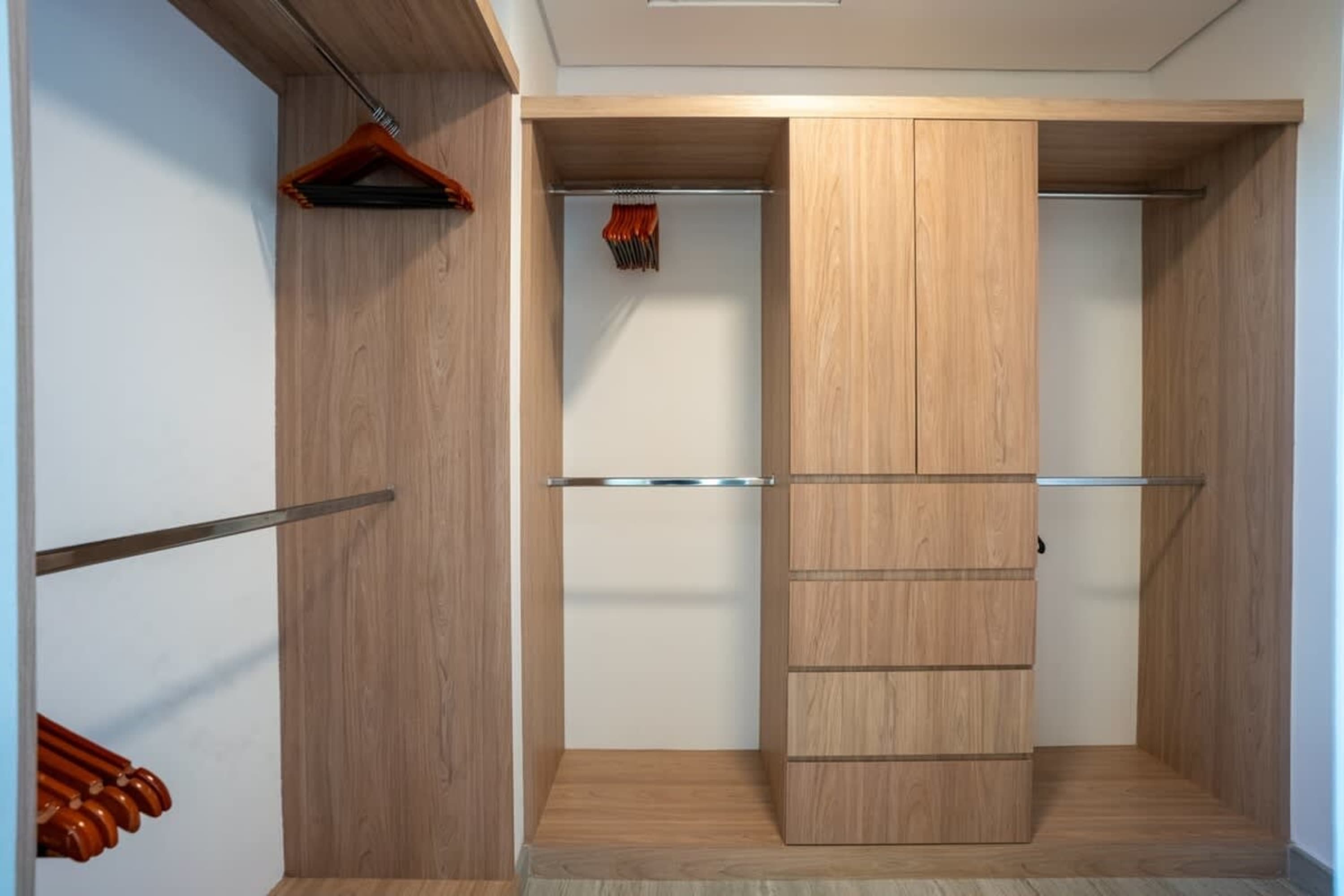 A modern wooden walk-in closet with clothes hangers and hanging rods.