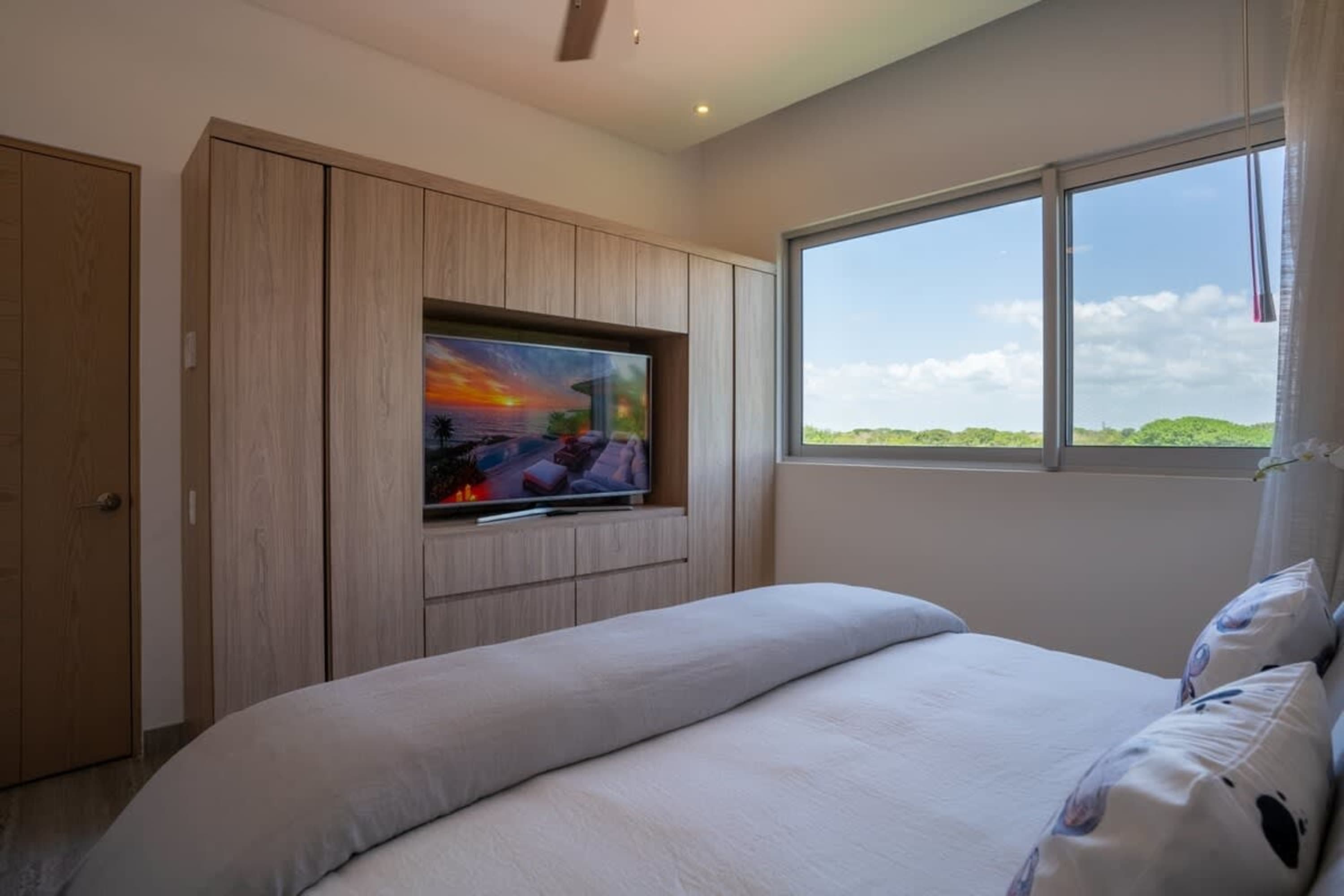 Modern bedroom with a large television built into a wooden cabinet and a window with a view of green