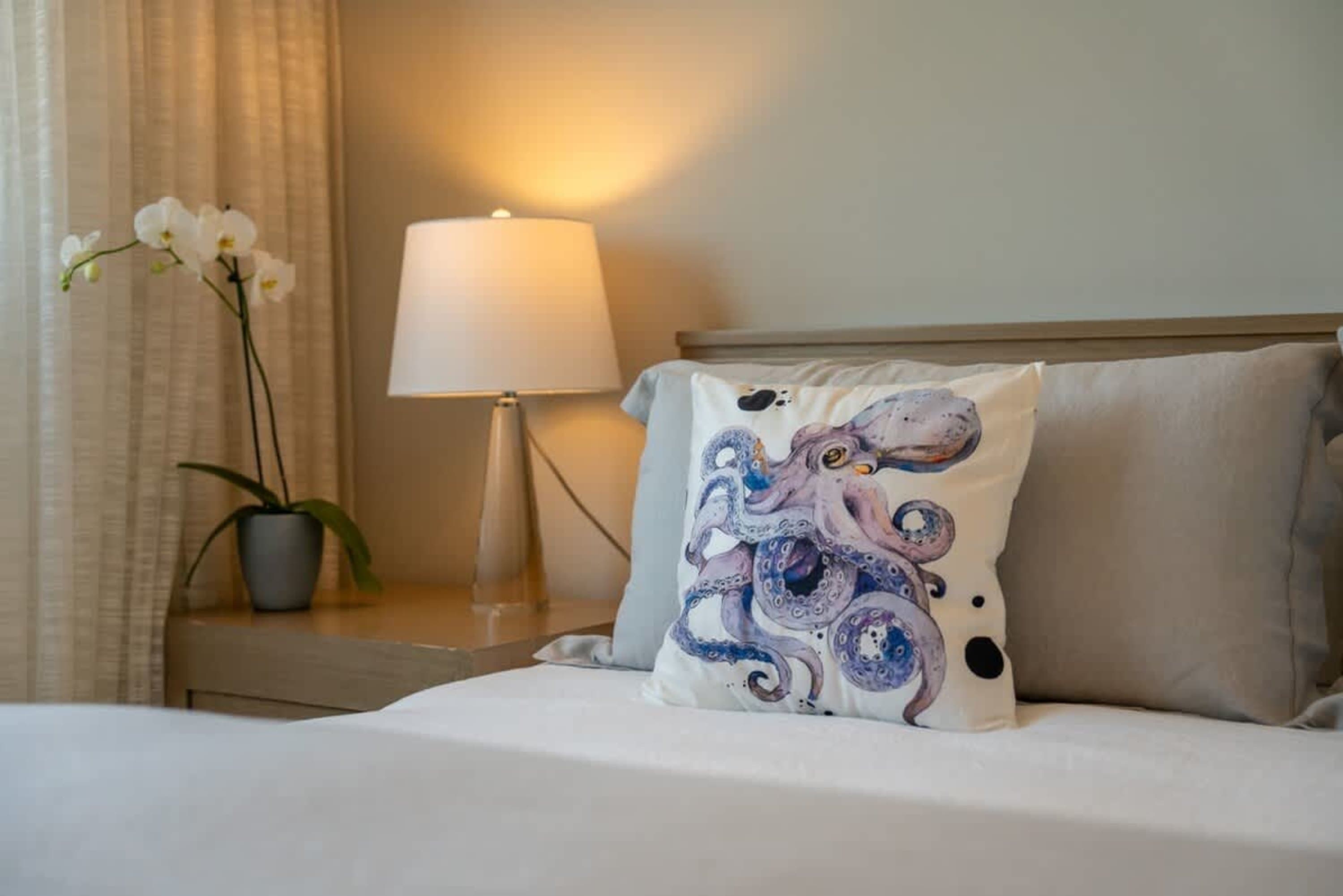 A white pillow with a purple octopus print sits on a bed next to a beige pillow.