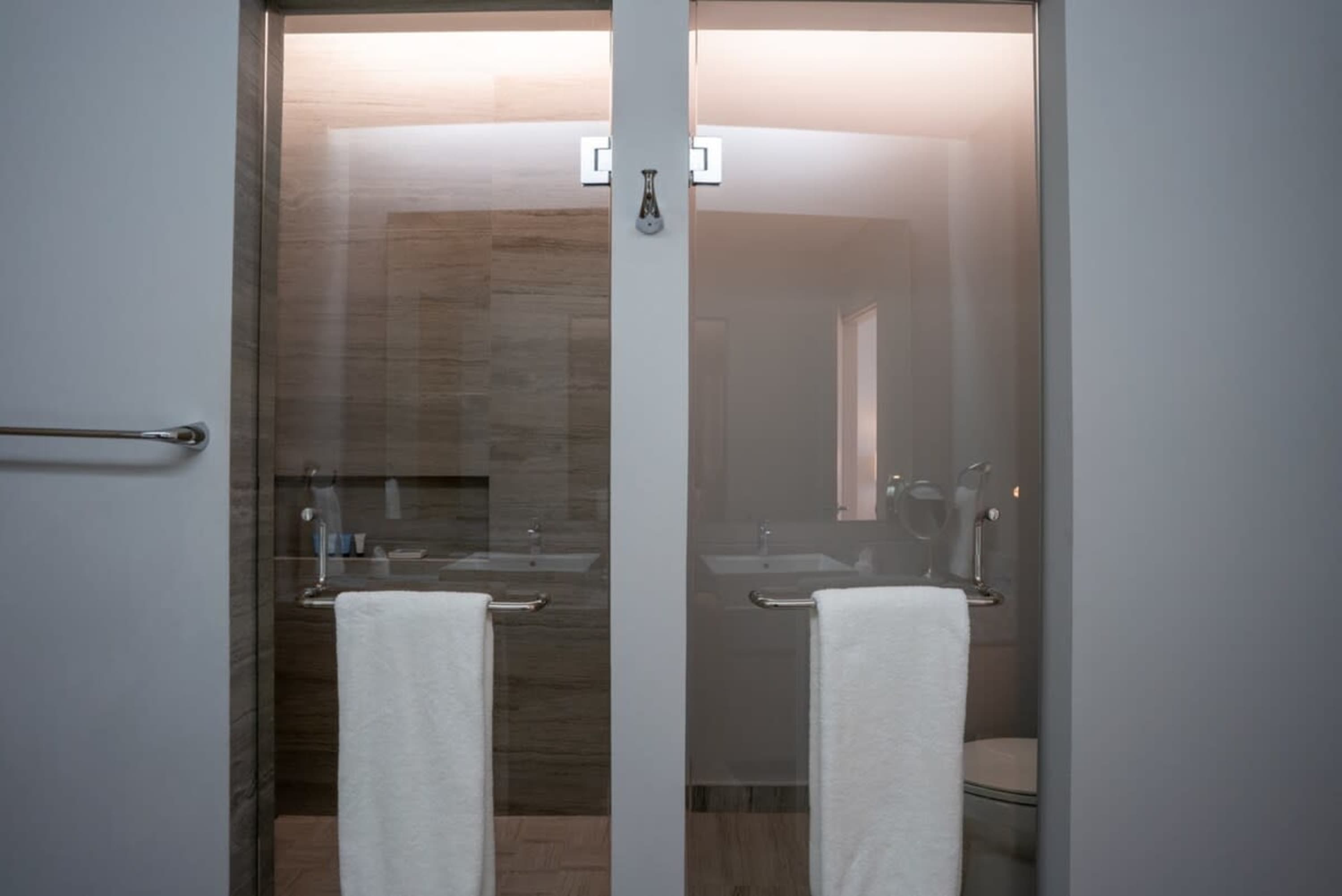 Two modern glass shower stalls with towels.